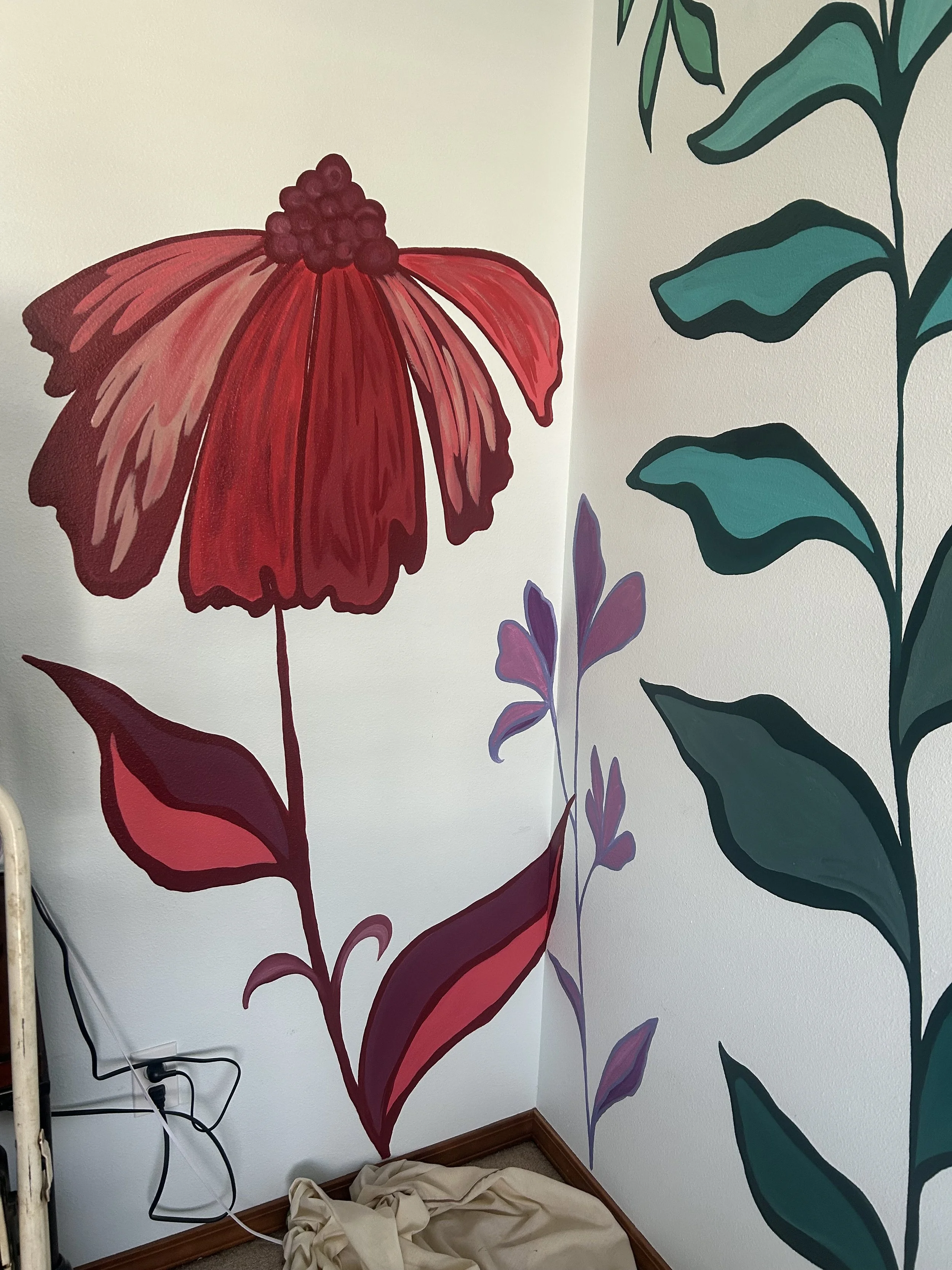 Interior view of a room with painted floral wall mural. The mural includes a large red flower with detailed petals and a cluster of small red berries at the center, along with green and purple leaves and smaller flowers. There are electrical cords and a cloth on the floor.