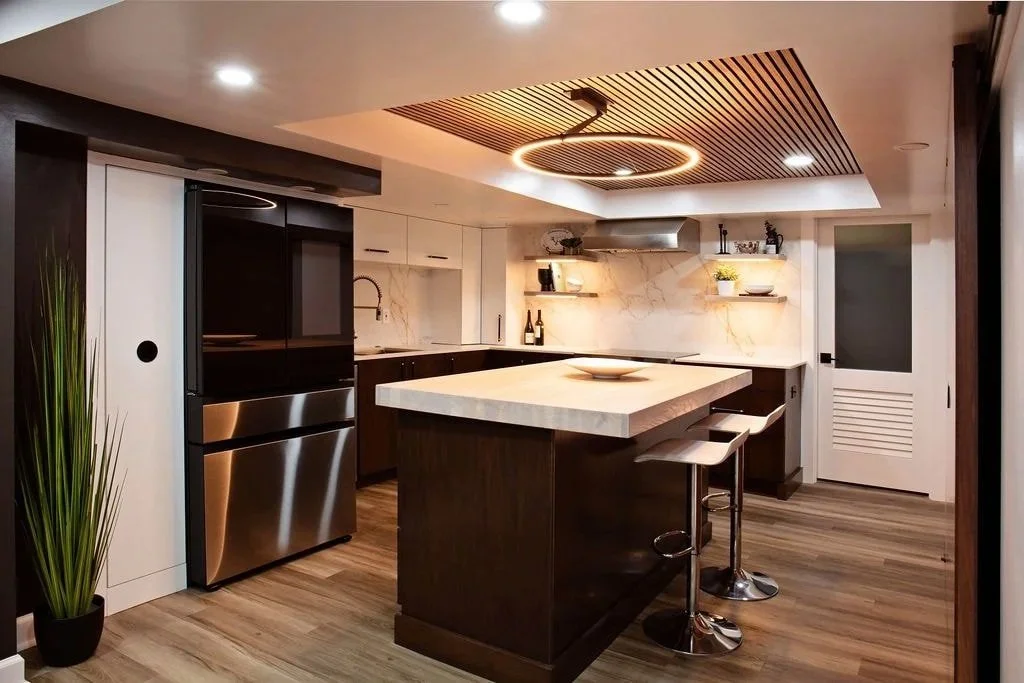 Modern kitchen with a central island, white marble countertops, black and white cabinetry, wooden flooring, and a decorative ceiling light fixture.
