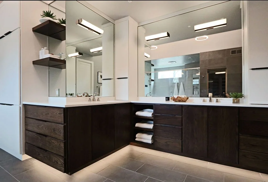 Primary bathroom double vanity with dark wood cabinetry, floor-to-ceiling storage, and sconce and toe kick lighting