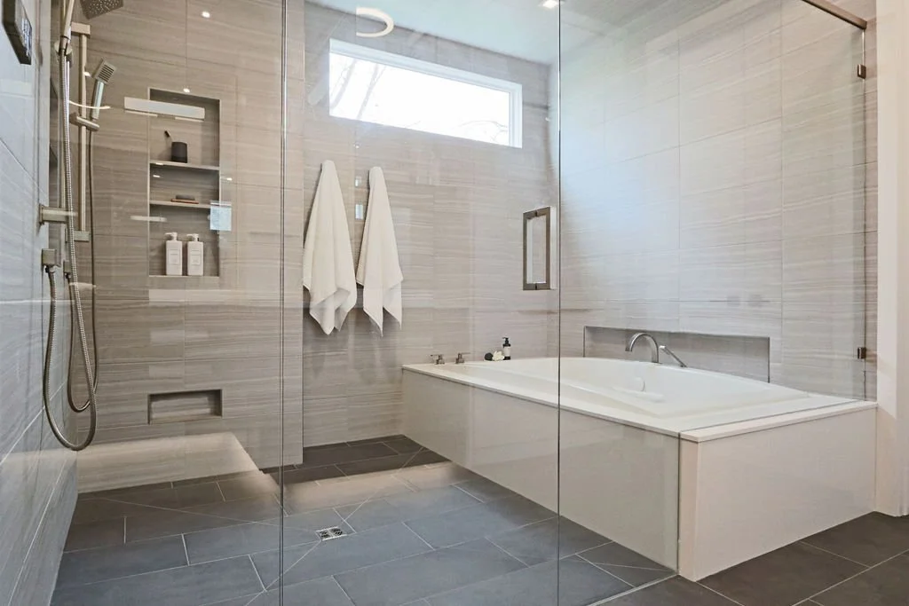 Zero-entry glass shower with tiled walls and a hydrotherapy tub with quartz surround, in a primary bathroom renovation