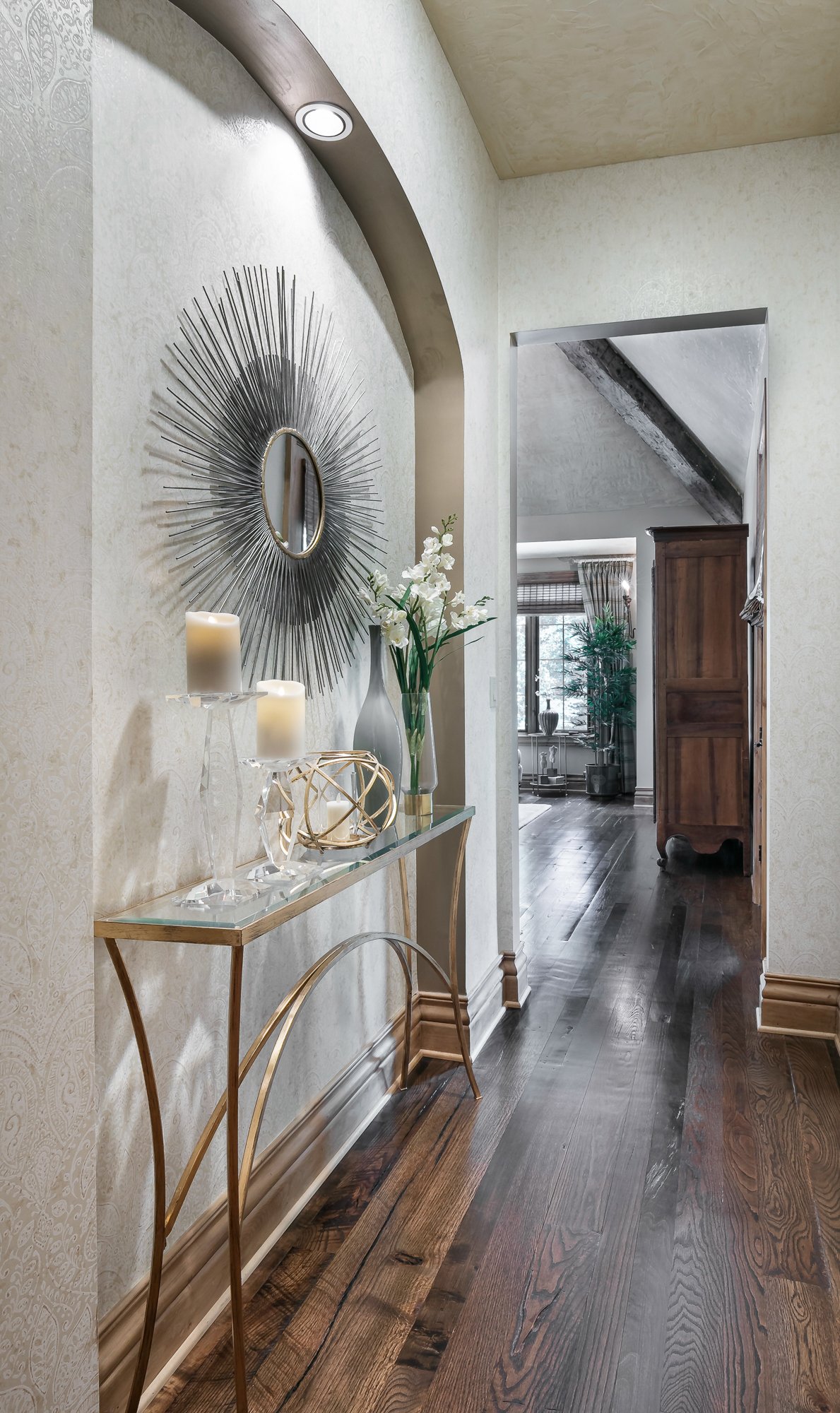 French Country entry hallway with gold console table and sunburst mirror leading to primary suite, Overland Park, Kansas.