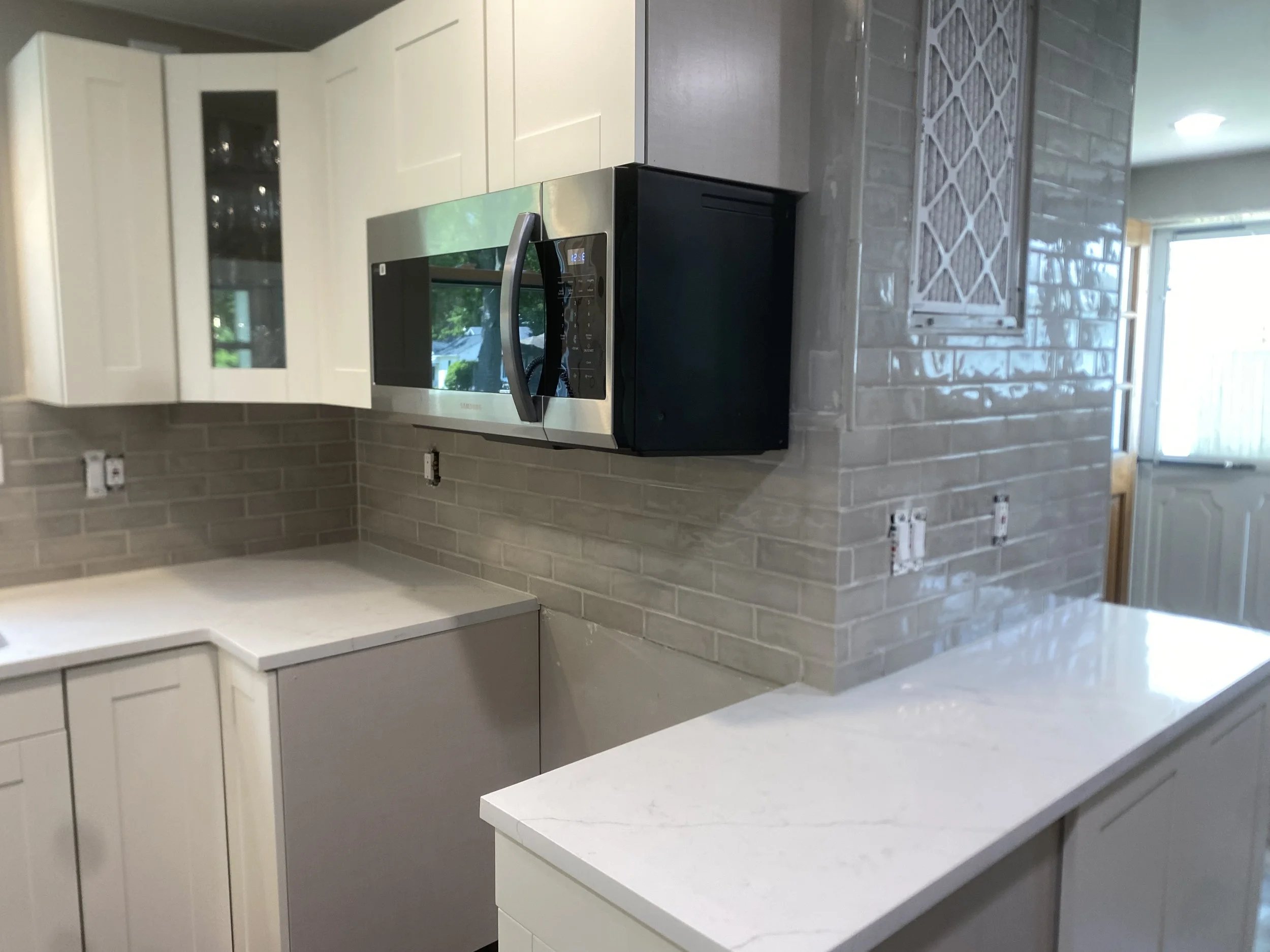 Modern kitchen with white cabinets, a stainless steel microwave oven, a white countertop, and beige tile backsplash.