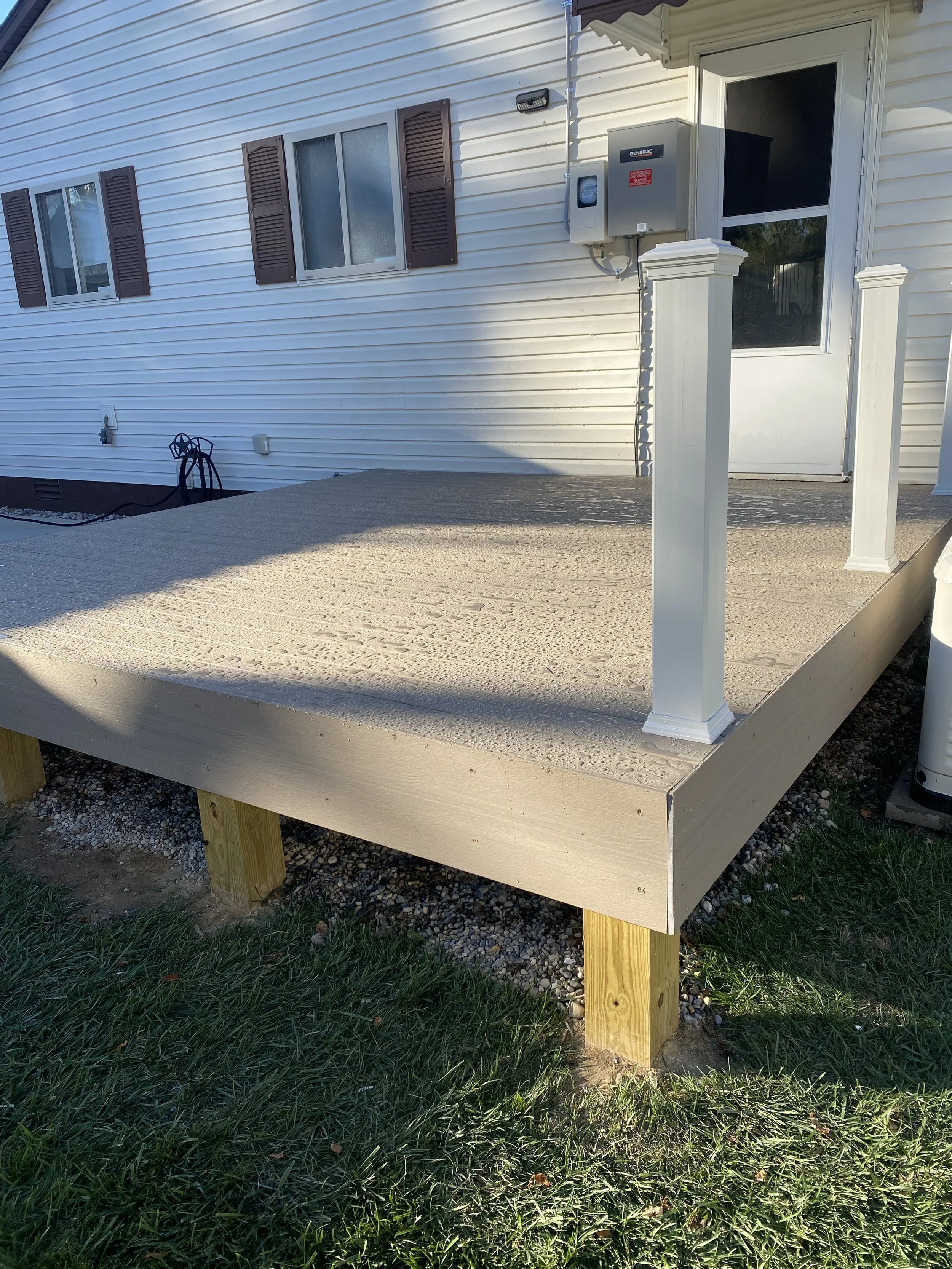 Newly built small elevated deck with white railing posts outside house with white siding and purple shutters.