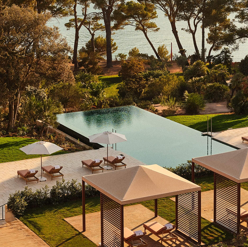 Poolside area with lounge chairs and umbrellas overlooking a lush garden and ocean.