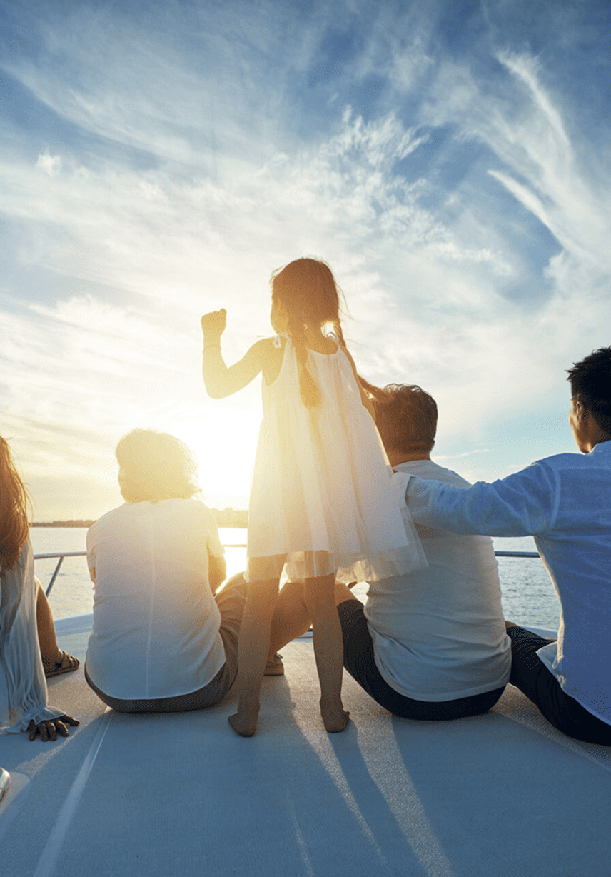 A girl standing on a boat at sunset, surrounded by seated adults, with a bright sky and clouds in the background.