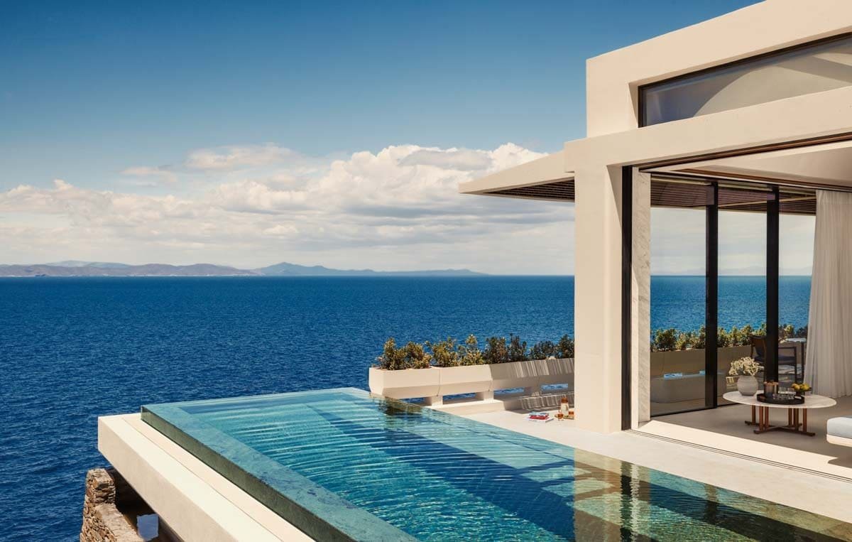 Modern oceanfront house with infinity pool overlooking the sea under a partly cloudy sky.