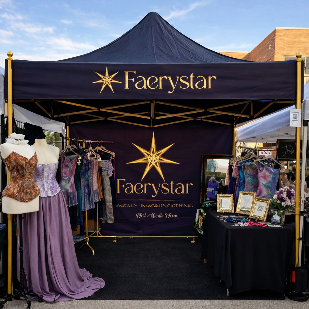 A fantasy-themed clothing and jewelry booth called 'Faerystar' with purple and gold decorations, displaying dresses on mannequins and racks, and framed jewelry on tables.