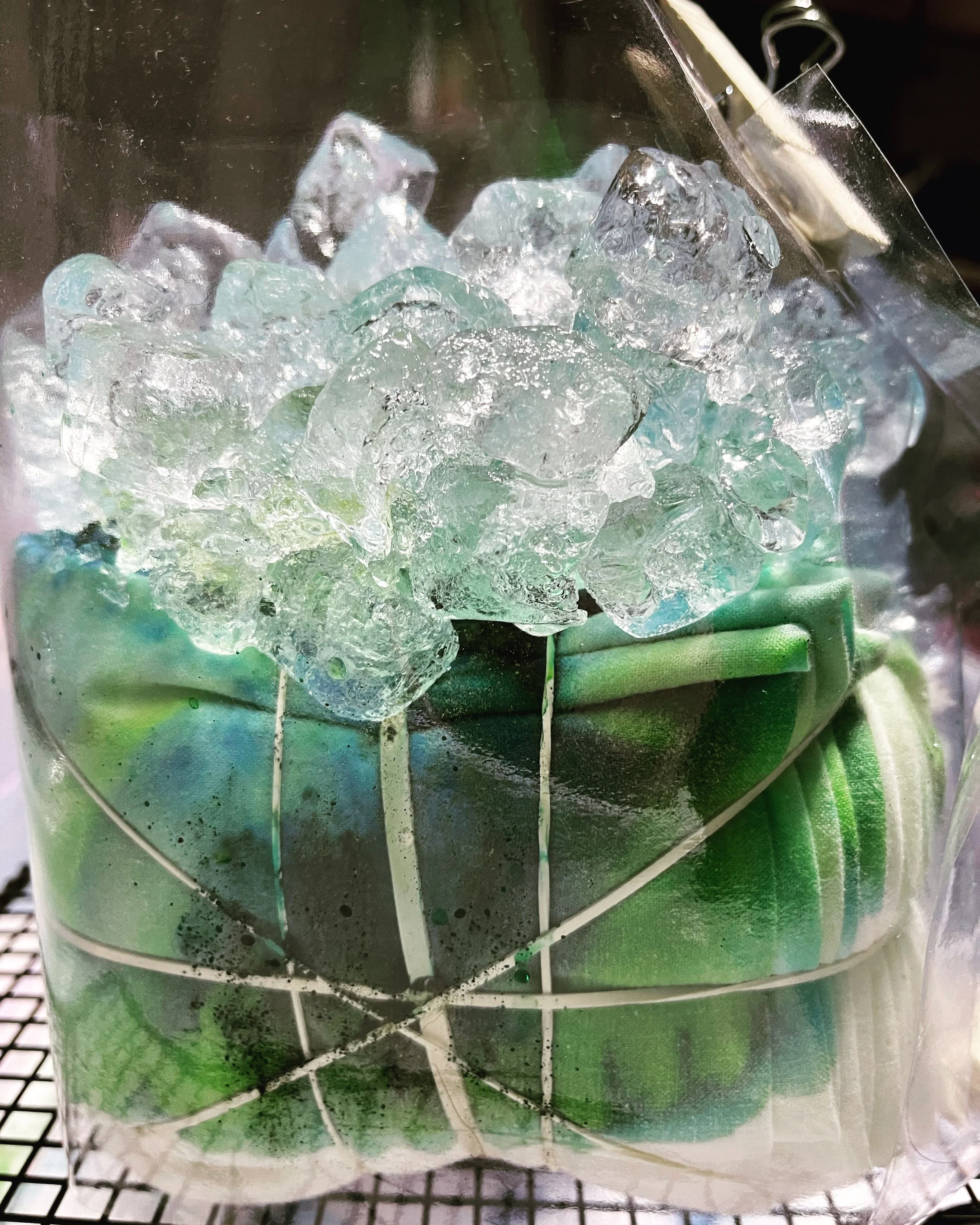 Close-up of a transparent container with crushed ice and small discarded pieces of plastic or paper, with a mesh surface underneath.