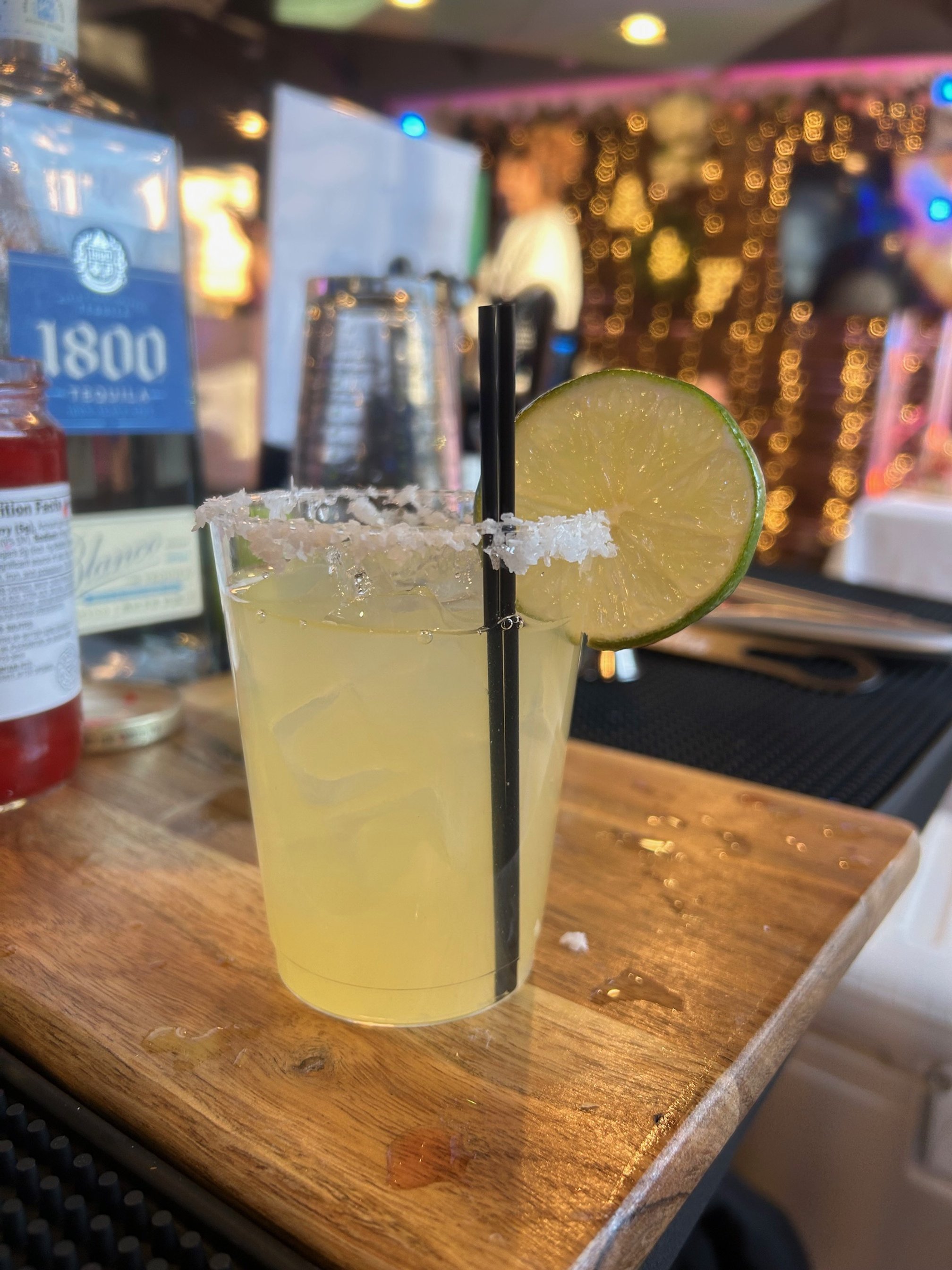 A margarita with a salted rim and lime slice on a wooden surface, with a tequila bottle in the background.
