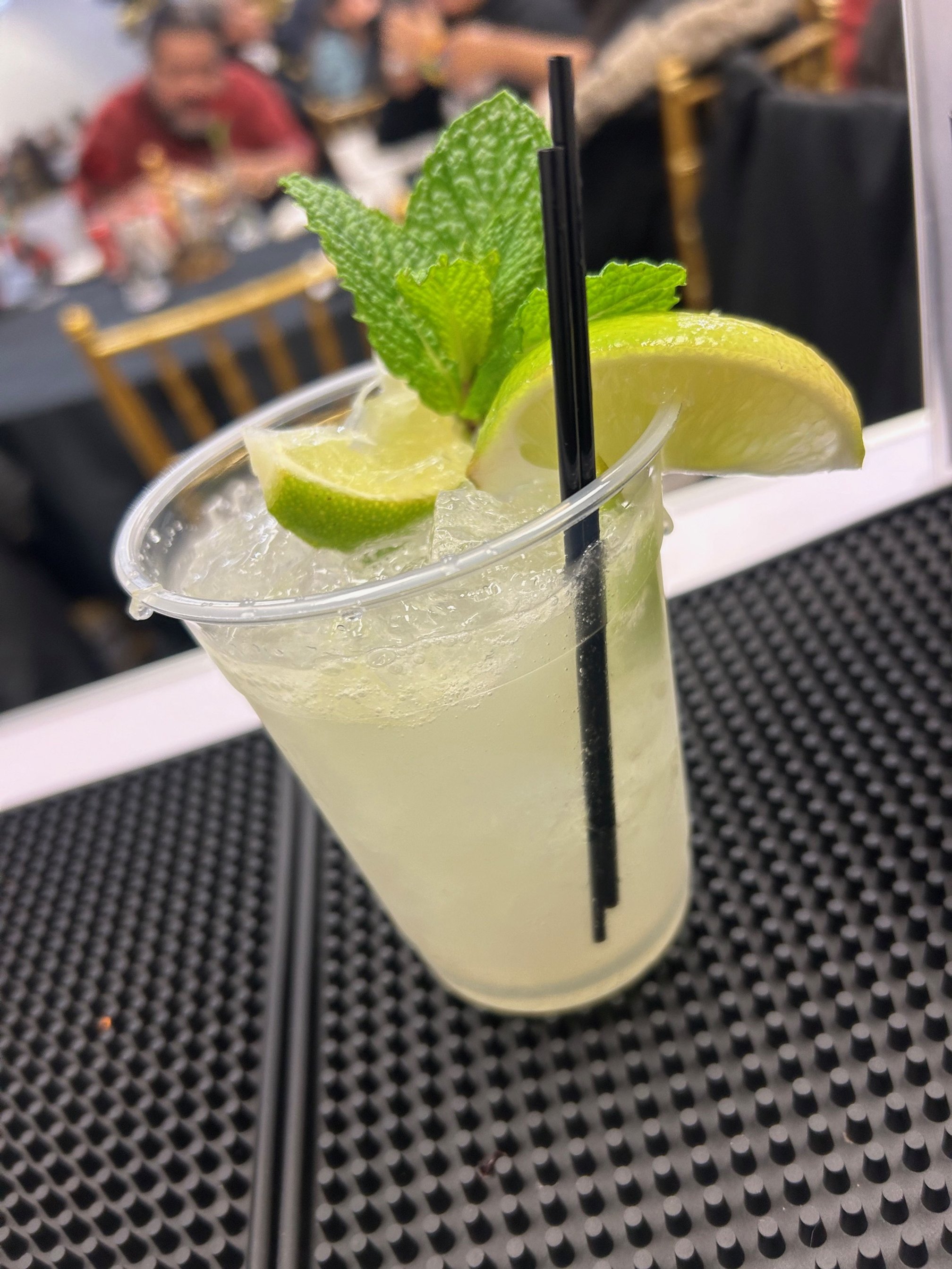 Iced cocktail in a plastic cup with lime, mint, and straws