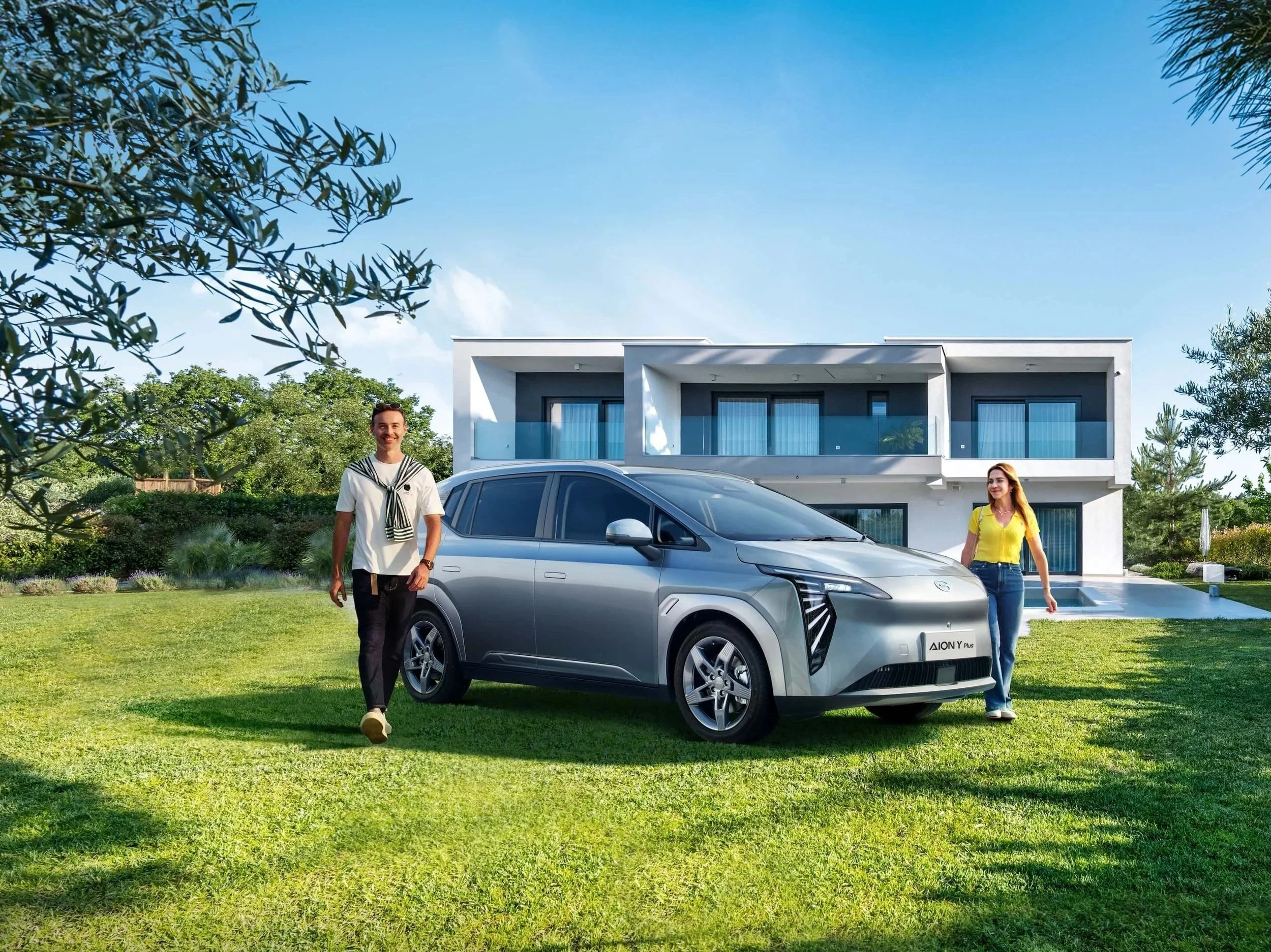 Una casa moderna con jardín, un coche plateado y dos personas, un hombre y una mujer, sonriendo frente a la casa, en un día soleado.