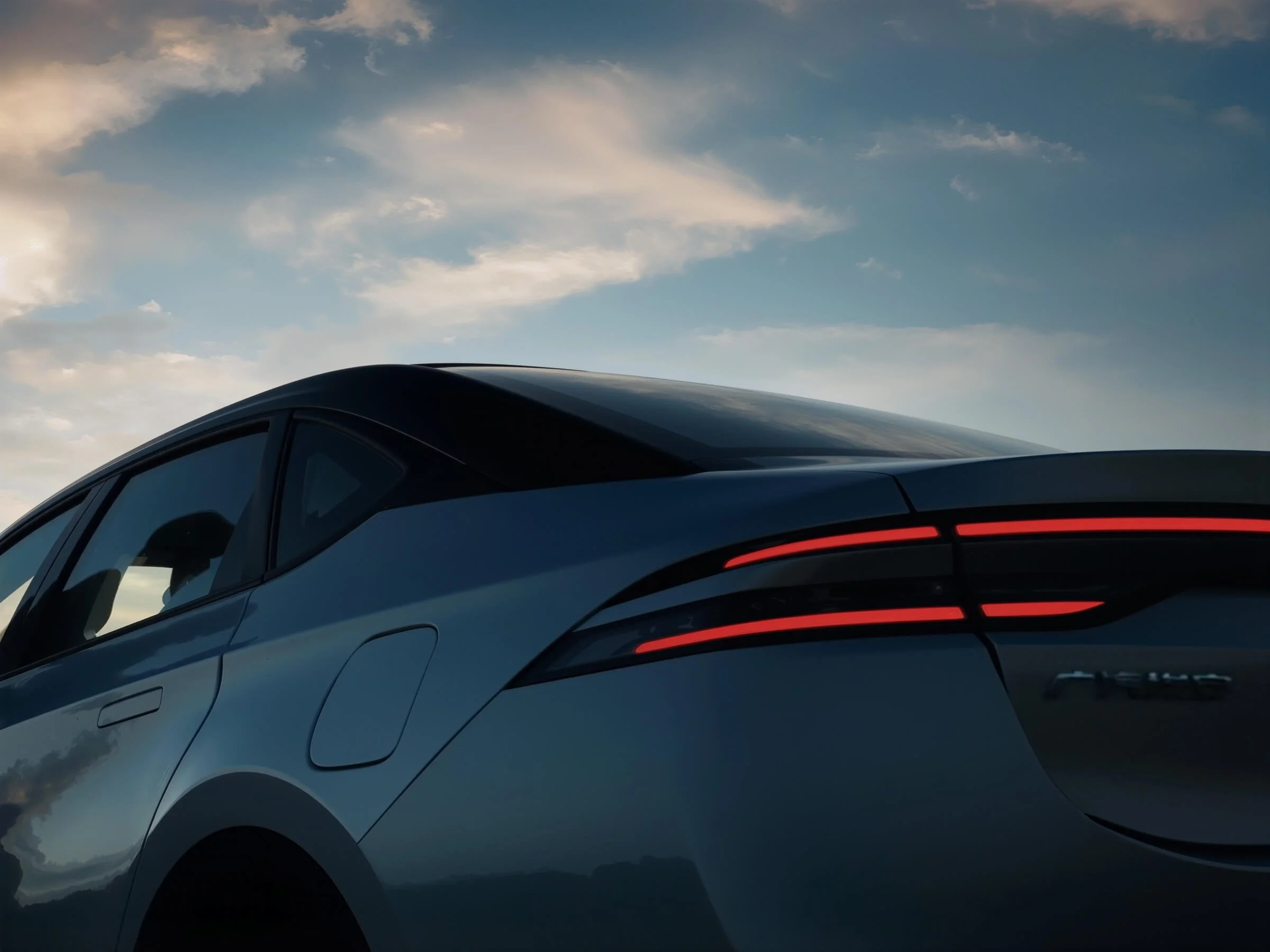 Vista lateral de un coche eléctrico negro con las luces traseras encendidas, bajo un cielo con nubes y un atardecer.