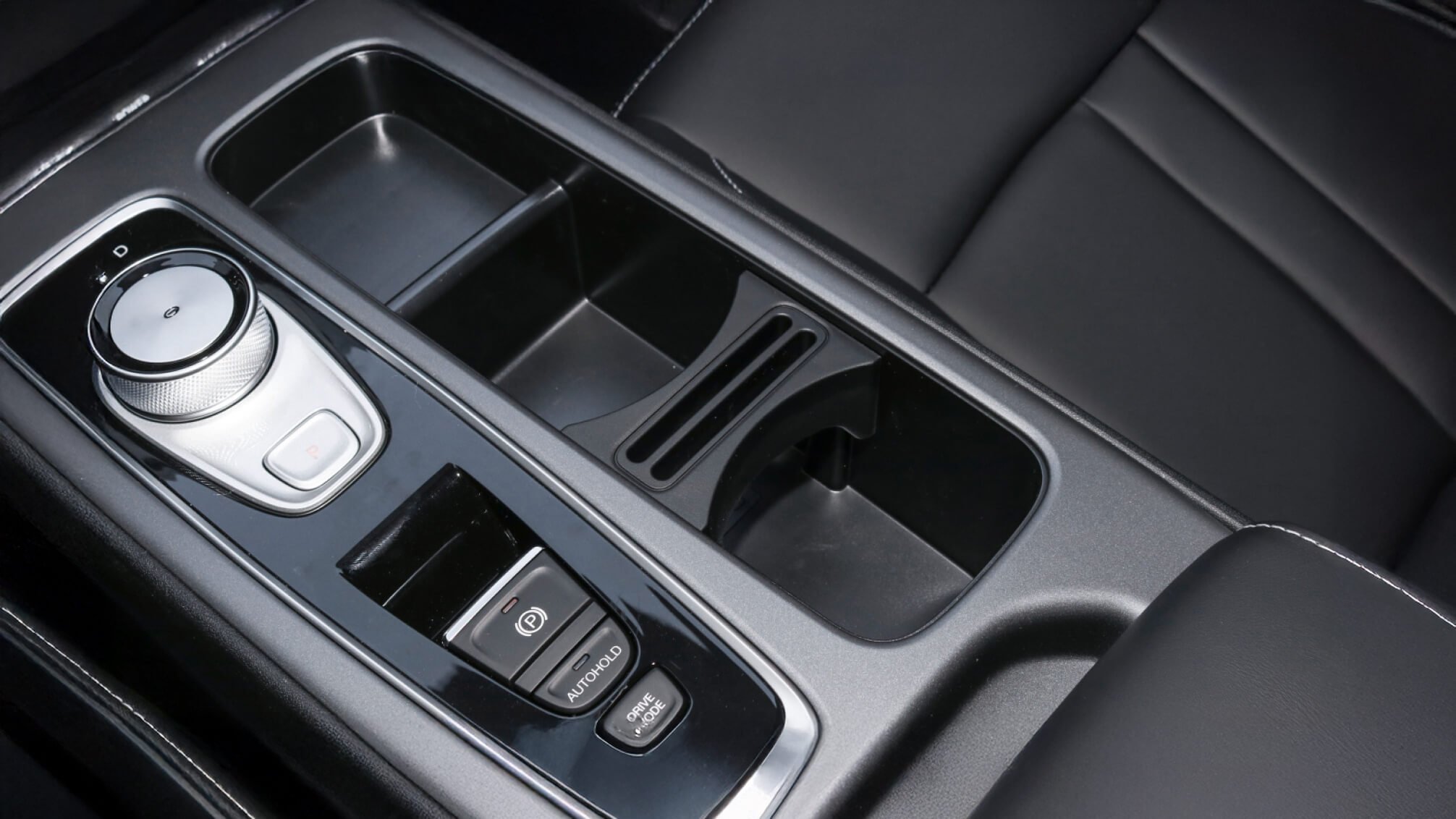 Consola central de coche con control giratorio, compartimentos de almacenamiento, botón de modo de conducción, y freno de mano electrónico.