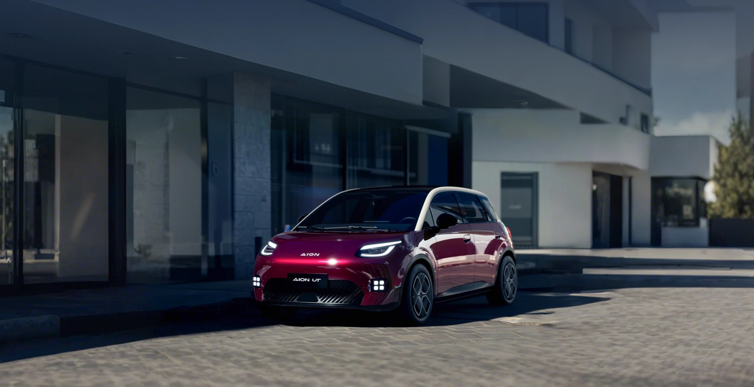 Coche eléctrico compacta de color rojo y negro estacionado en la acera frente a un edificio moderno