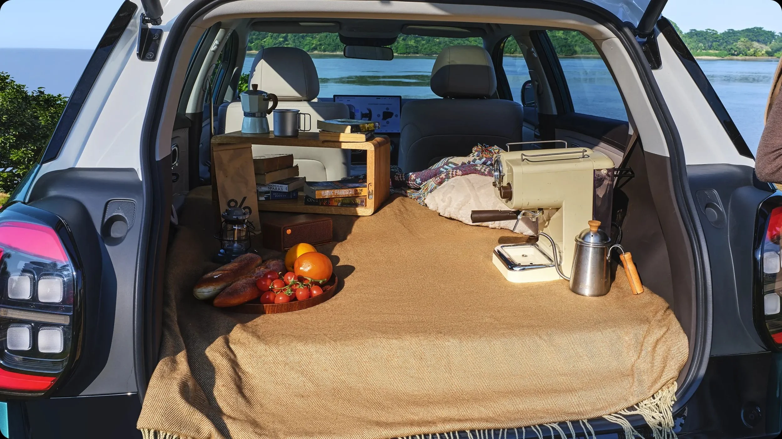 Interior de un coche convertido en campamento, con comida, libros y equipo de camping junto a un río.