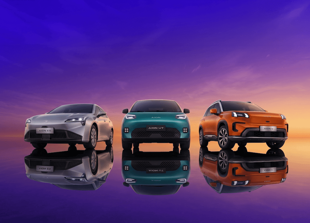 Tres autos eléctricos en línea en un paisaje con cielo al atardecer, reflejados en una superficie acuosa, de diferentes colores y modelos.