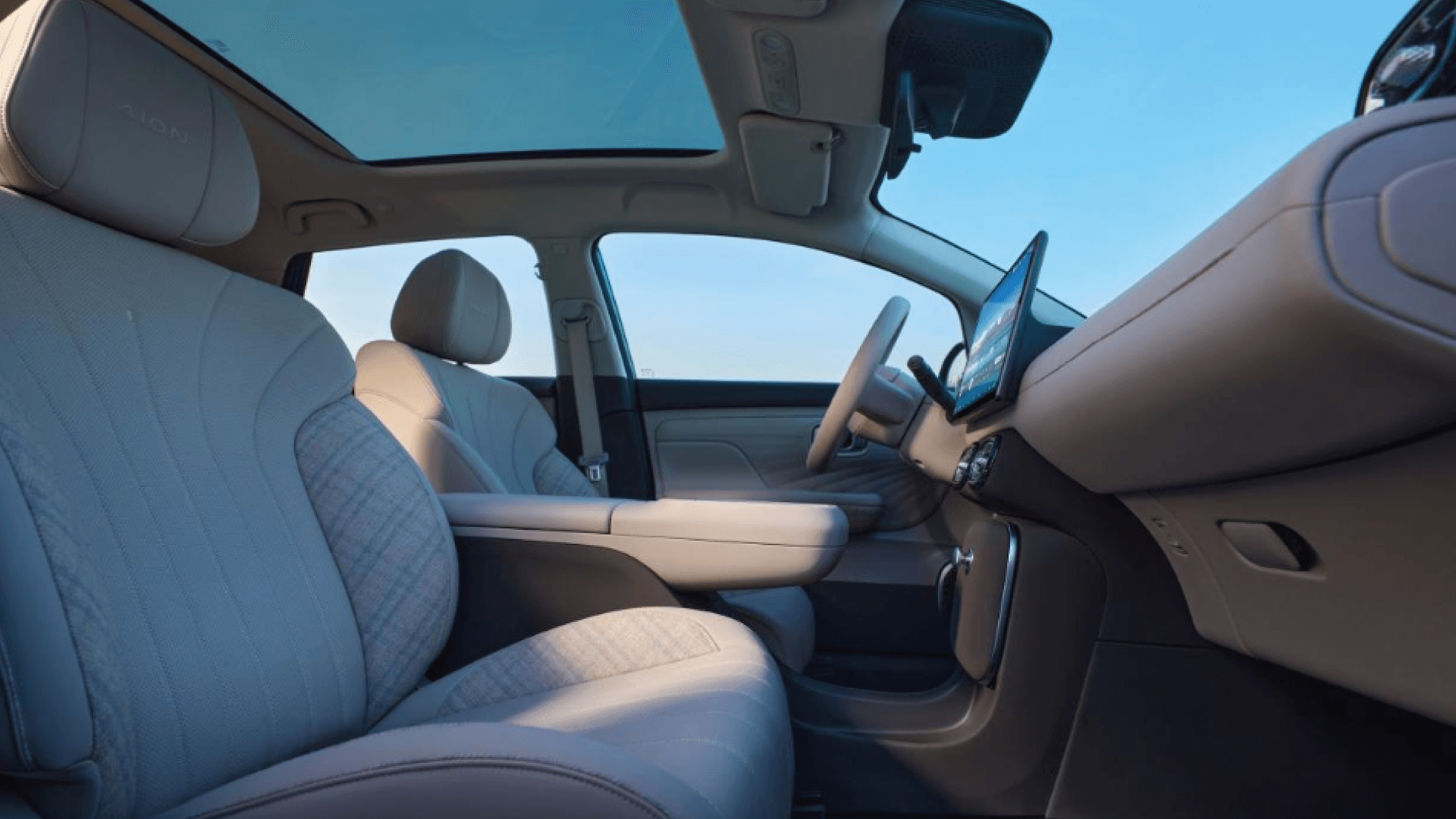 Interior de un automóvil con asientos beige, volante, pantalla táctil en el tablero y cielo visible a través del techo panorámico
