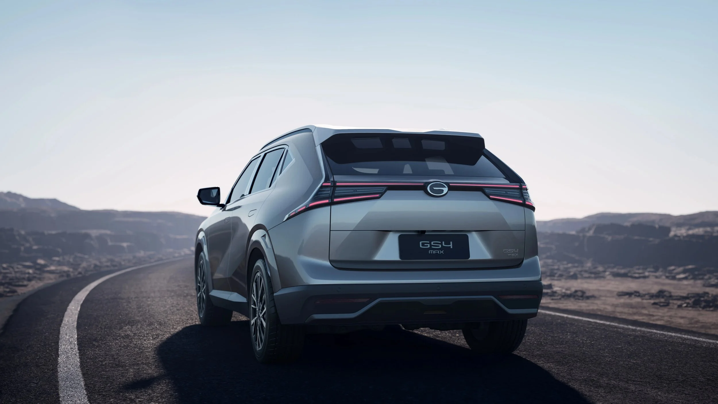 Vehículo eléctrico gris en una carretera desierta en un paisaje montañoso, vista trasera.