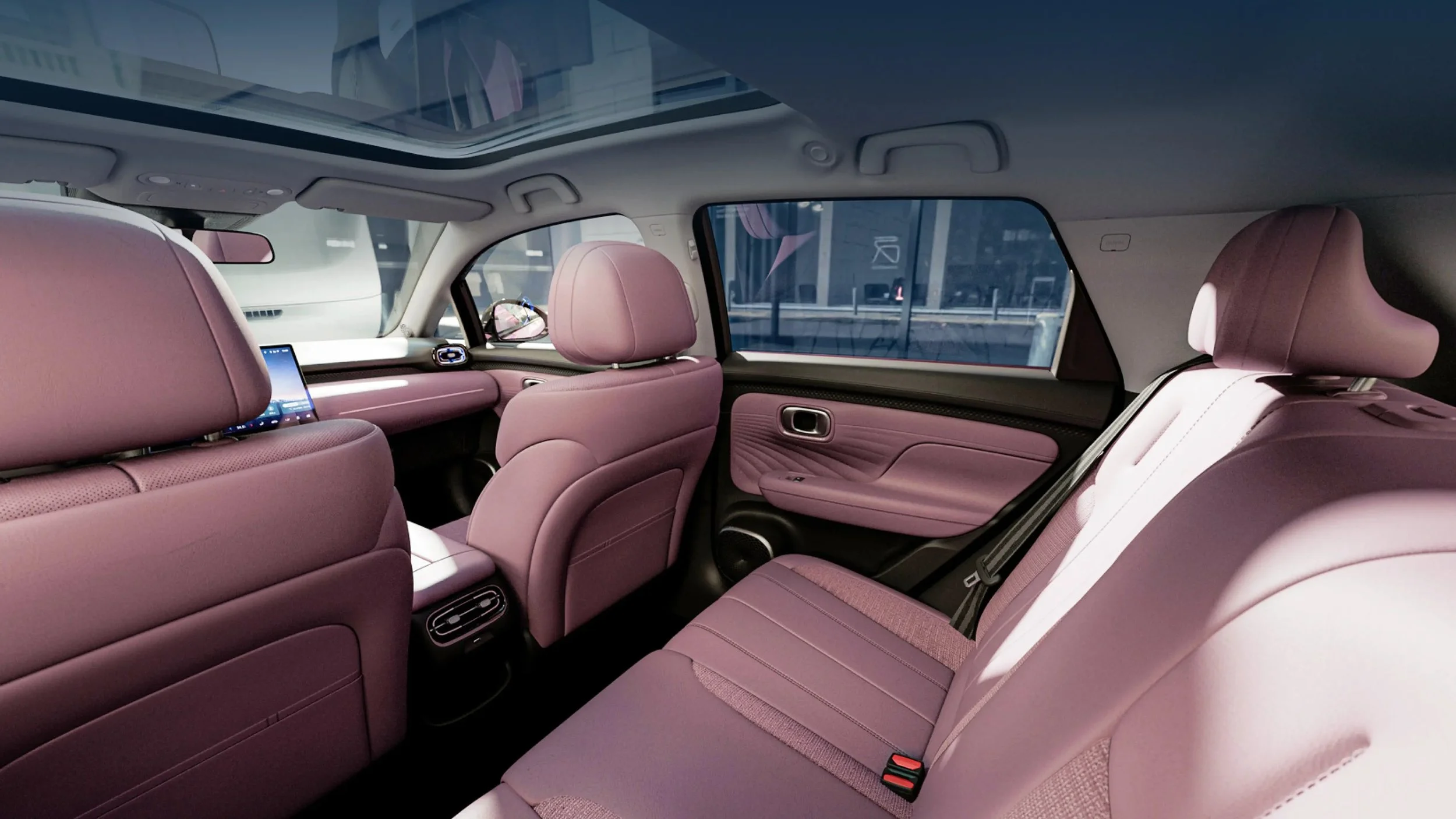 Interior de un automóvil con asientos y paneles en tonos rosa y detalles en negro, ventanas grandes, techos panorámicos y dispositivos tecnológicos visibles.