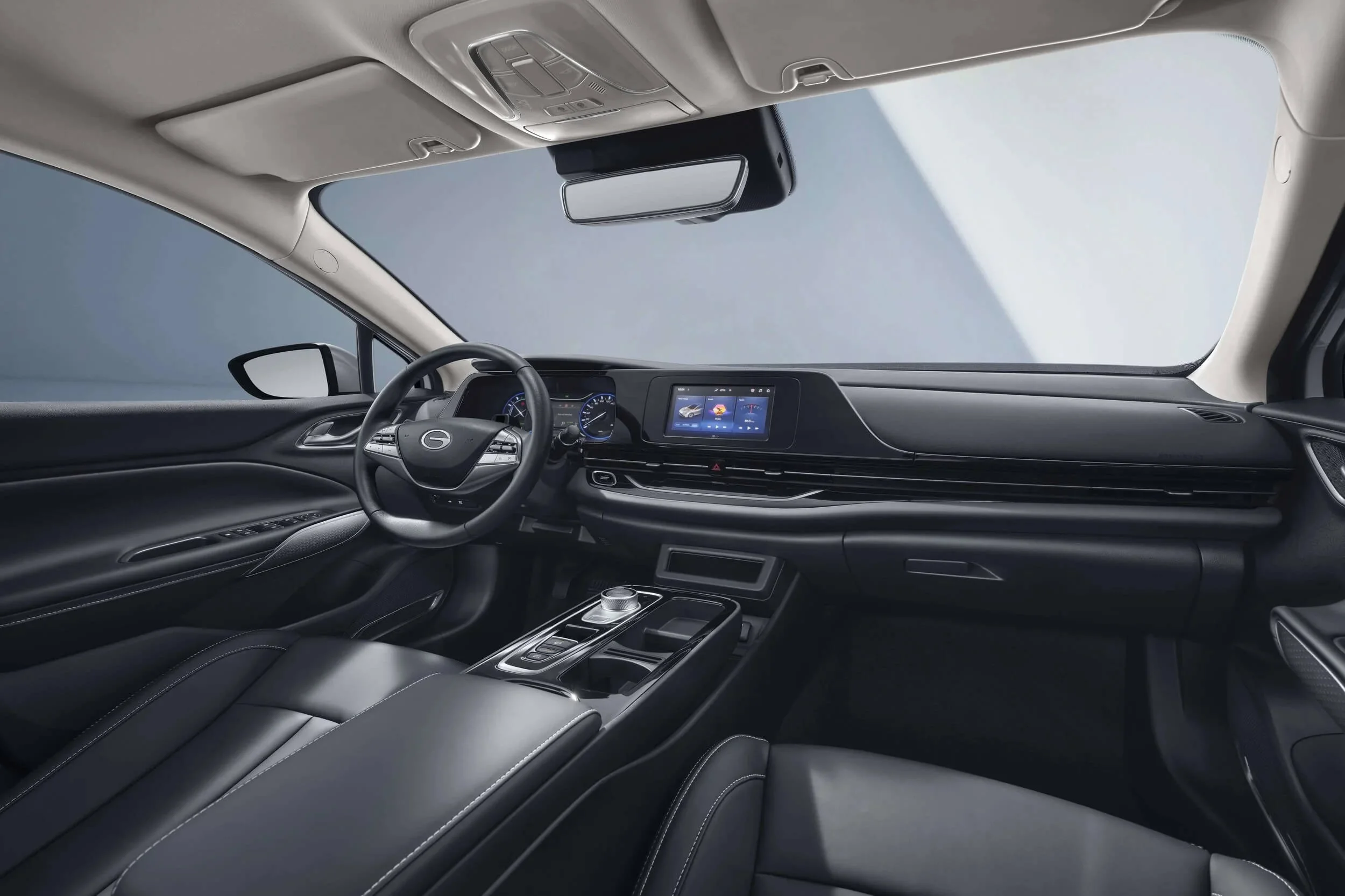 Interior de un coche moderno con volante, tablero digital, pantalla táctil central, consola con control de transmisión, asientos de piel y techo claro.