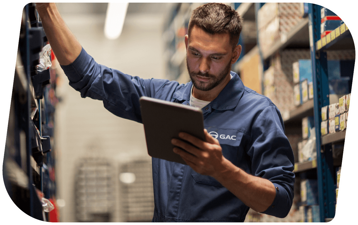 Un hombre con uniforme de trabajo, revisando información en una tableta en un almacén, rodeado de estanterías con productos.