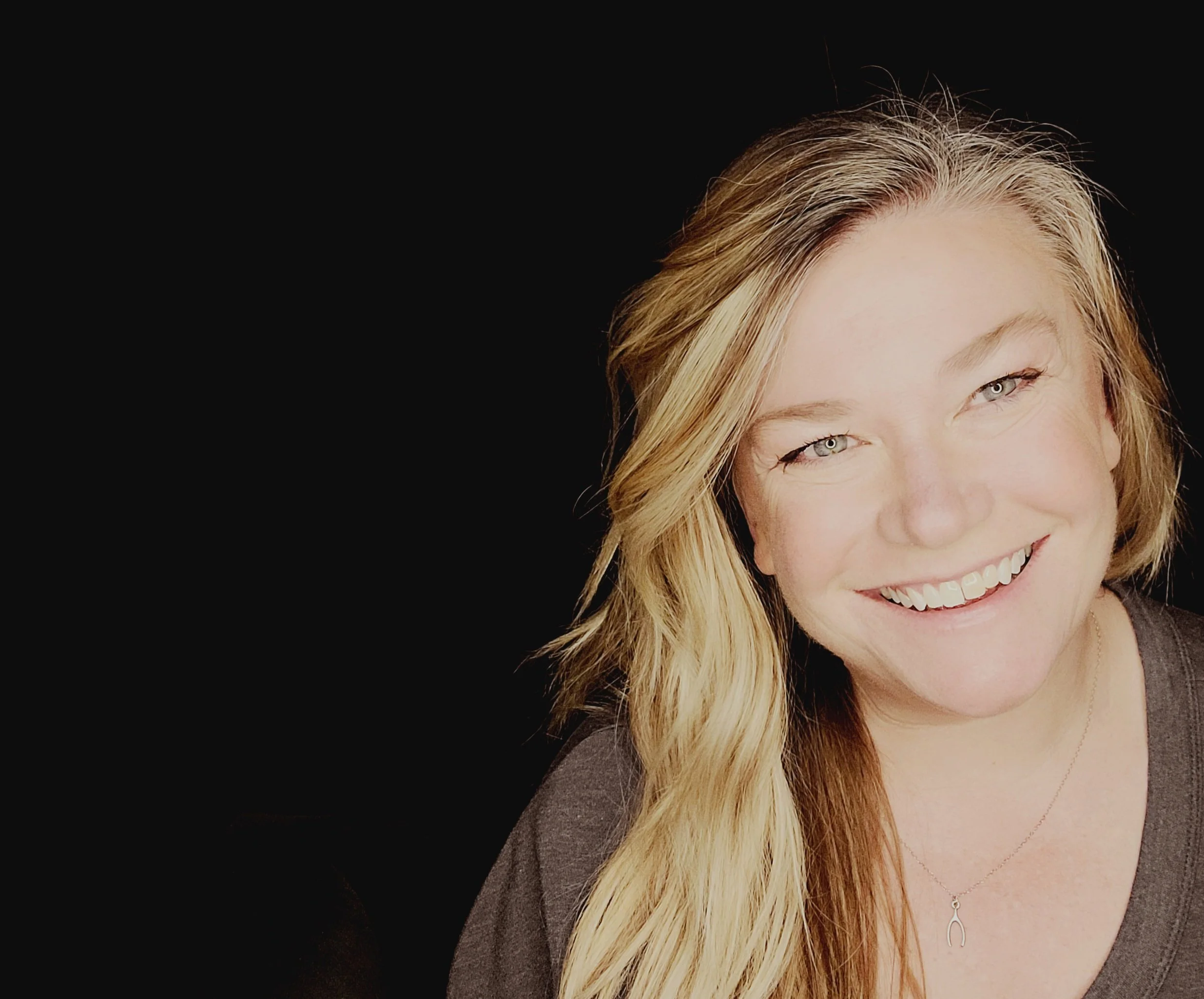 Half of a smiling woman's face (Ashley Foster) with blonde hair, set against a black background.