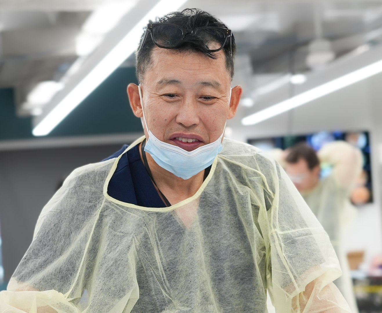 A man wearing a face mask and protective gown, appearing to be in a medical or laboratory setting.