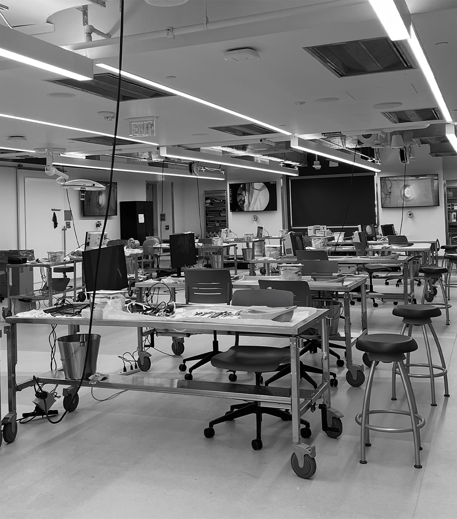 Empty hospital or medical facility room with empty beds, monitors, chairs, and medical equipment.