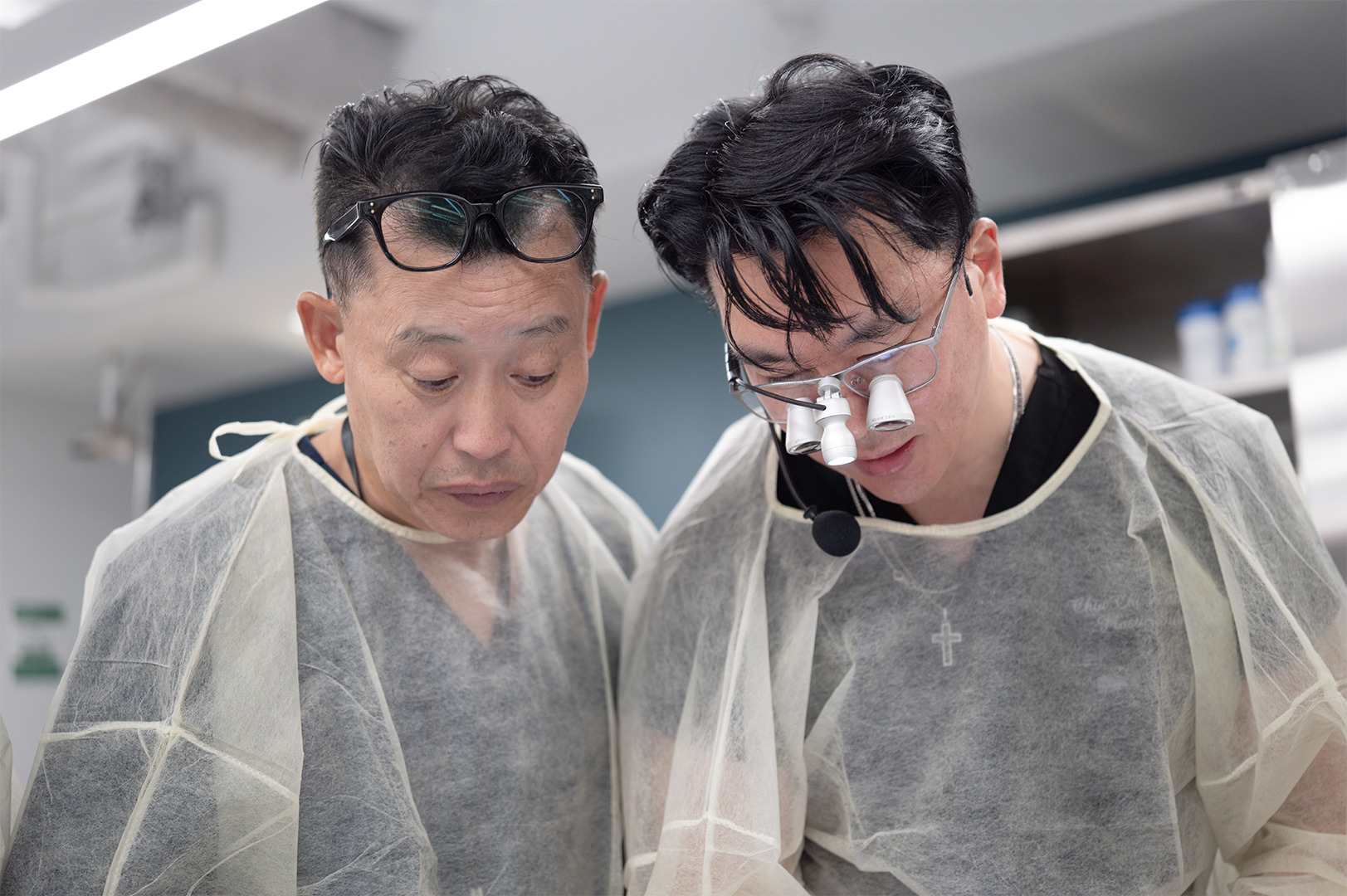 Two male doctors wearing magnifying glasses and surgical masks examining something.