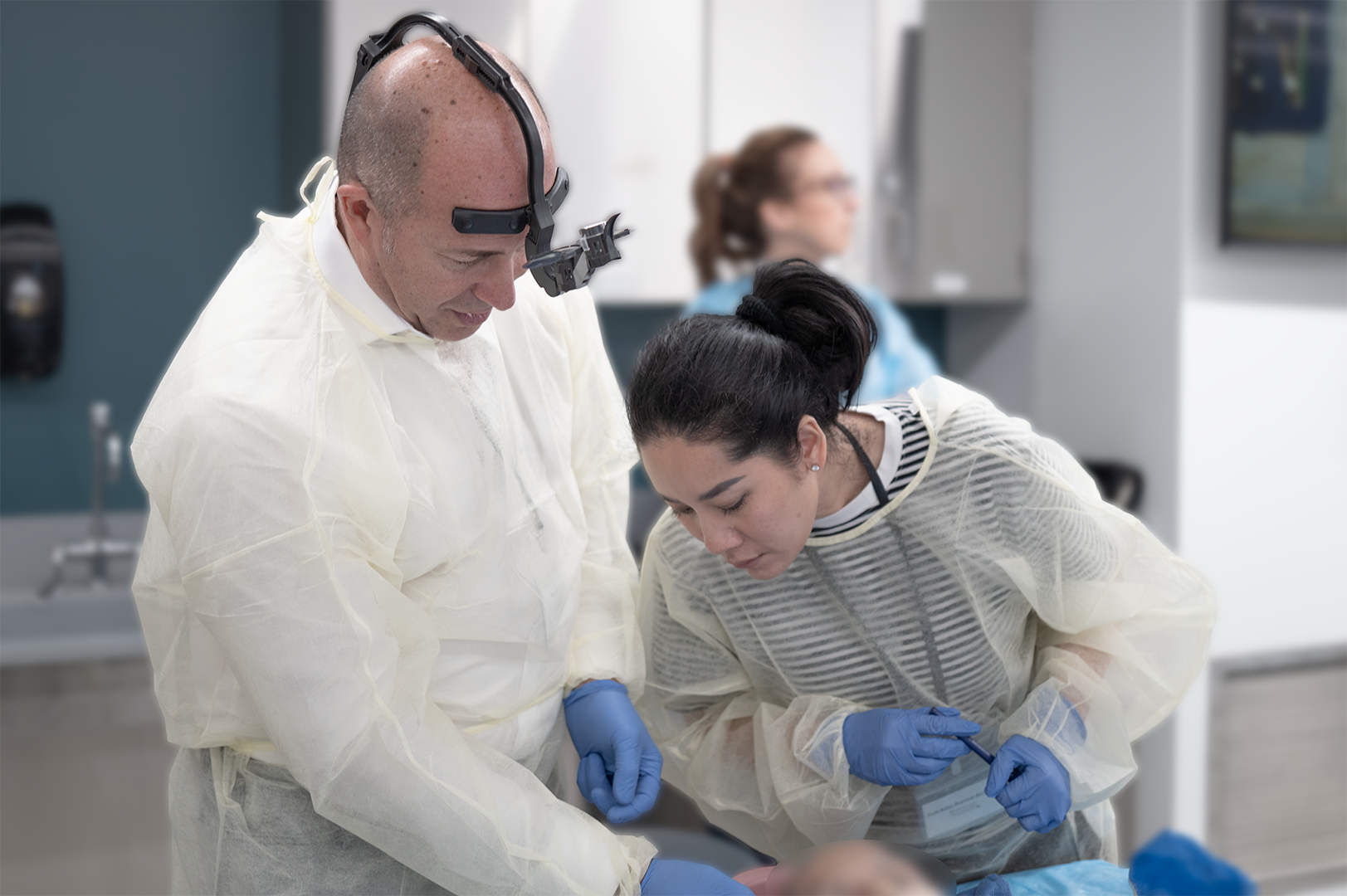 Medical professionals in protective gowns and gloves perform a procedure in a hospital or clinic setting.