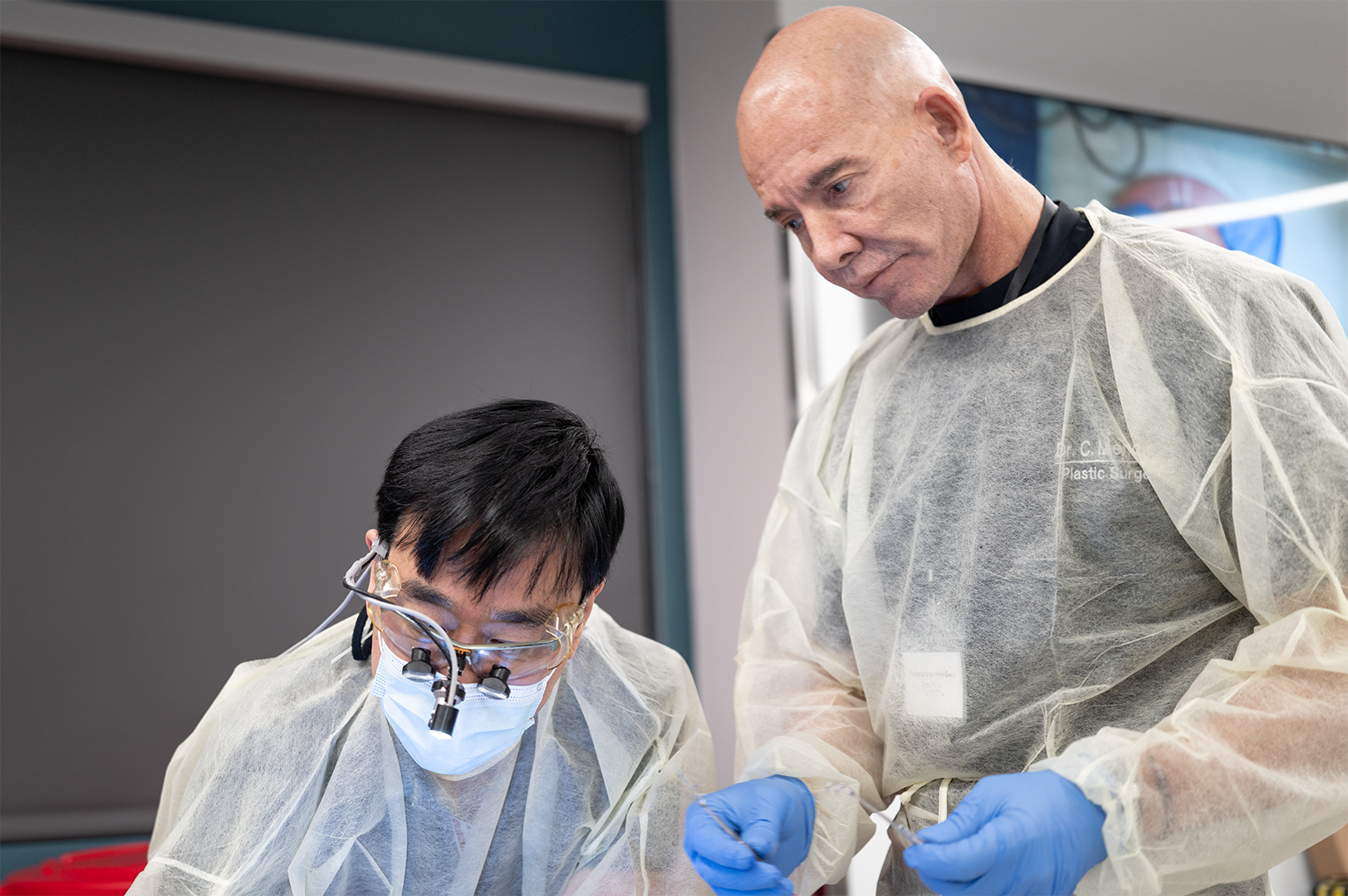 Two surgeons in protective gear, including gloves, masks, and magnifying glasses, performing a procedure in an operating room.
