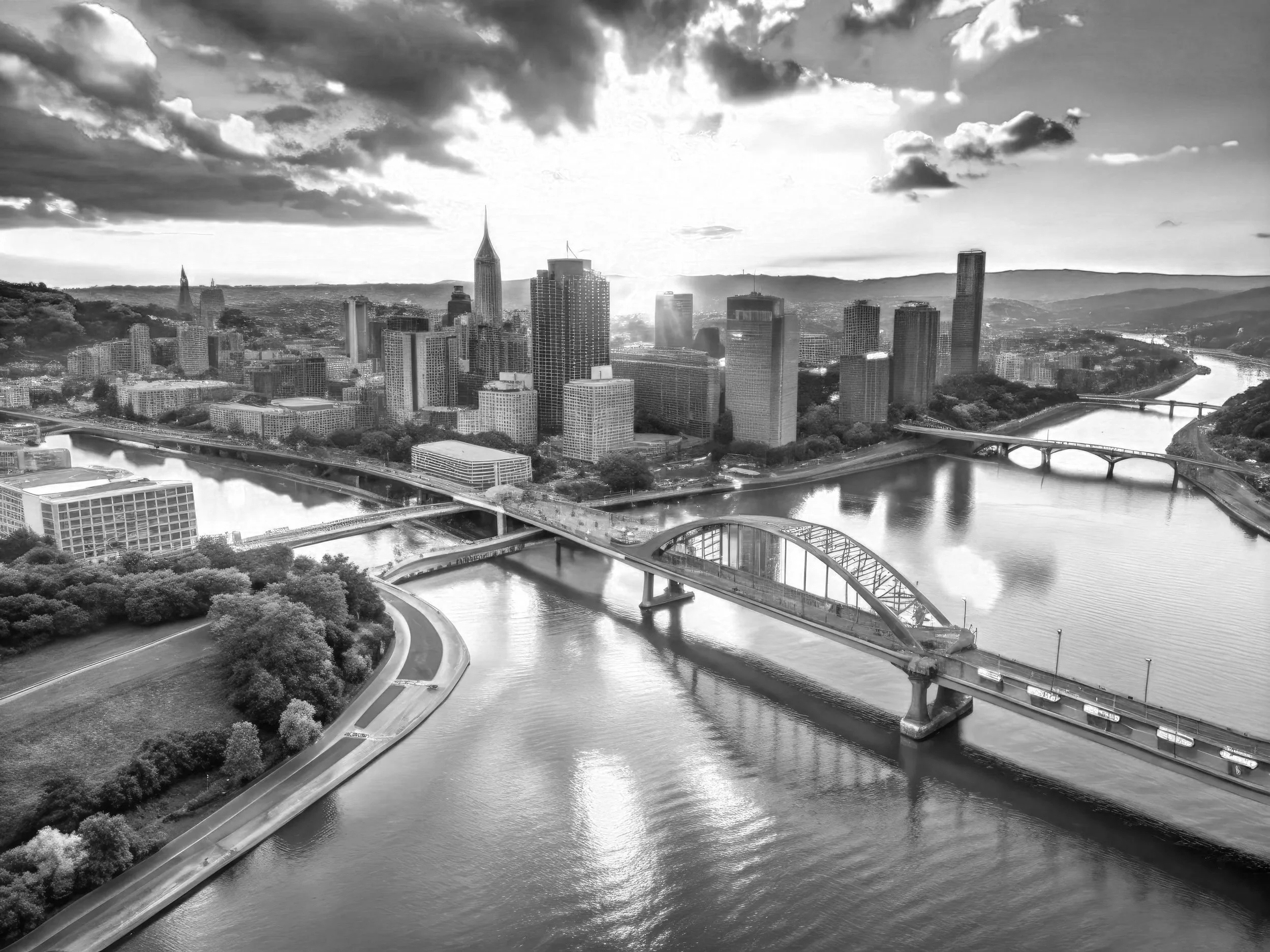 Black-and-white aerial view of downtown Pittsburgh, Pennsylvania, with skyscrapers, bridges over the Allegheny River, and surrounding hills in the background.