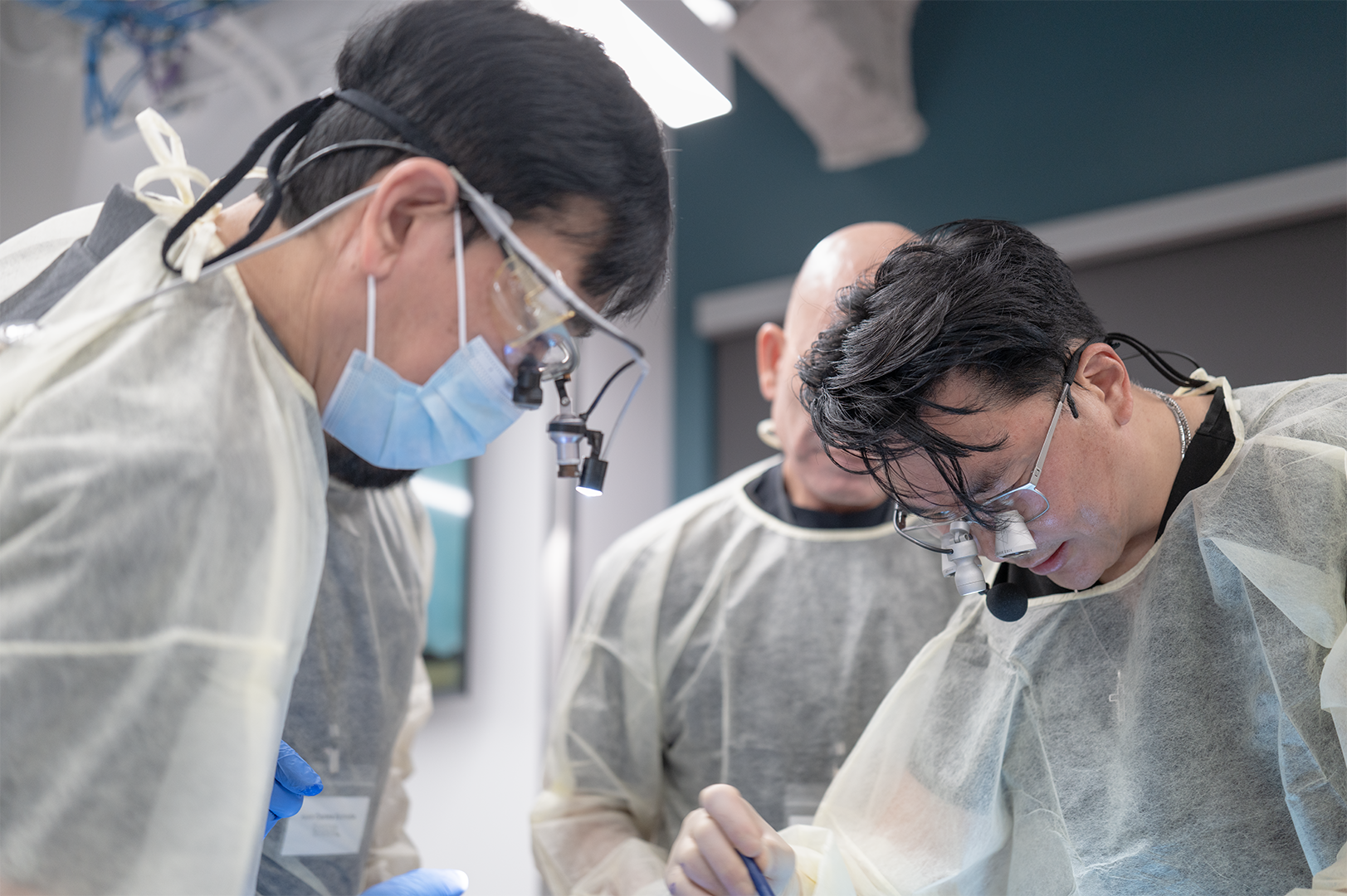 Three surgeons wearing protective gear, including magnifying glasses, masks, and gloves, performing a surgery in an operating room.
