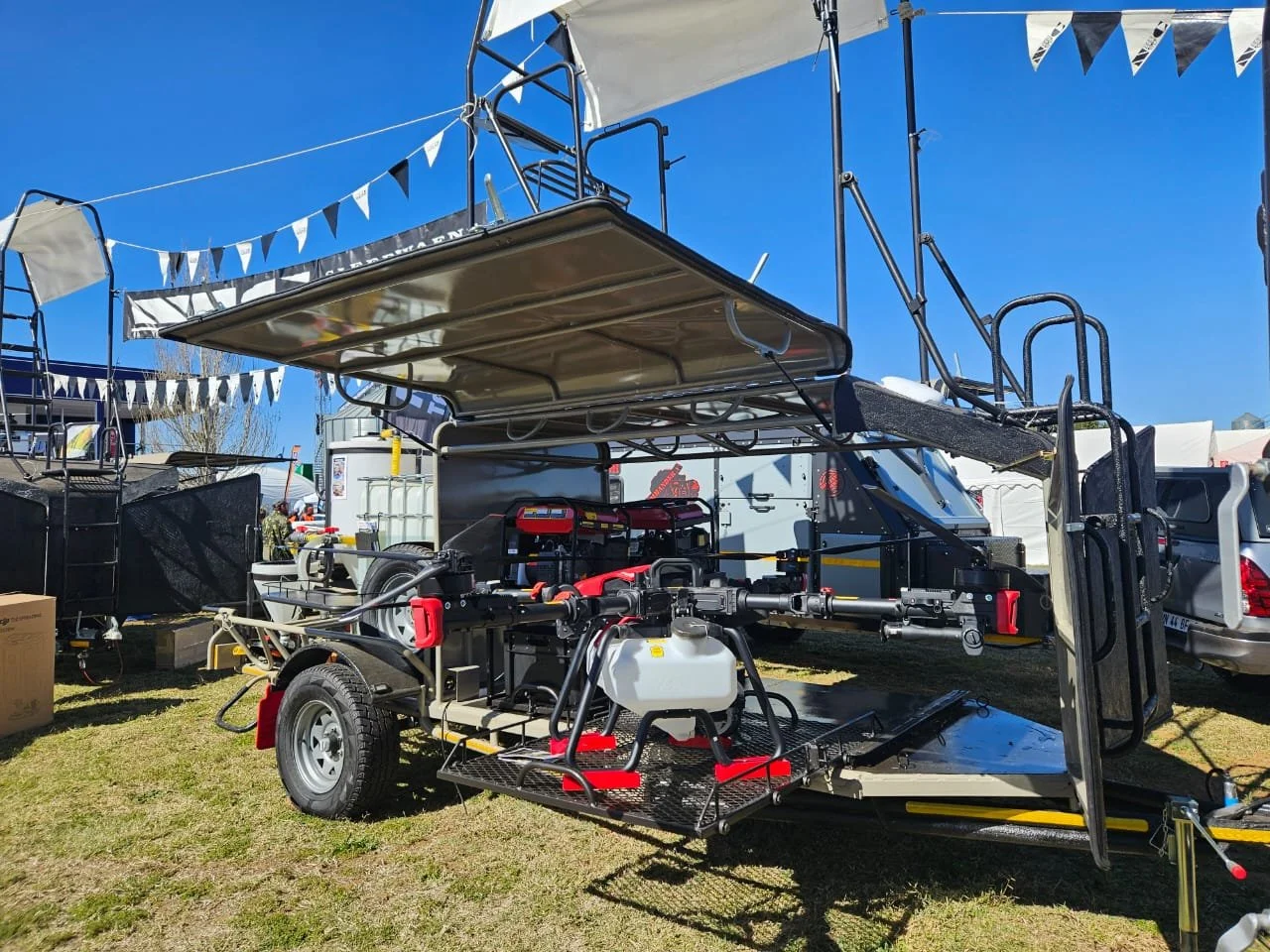 A boat trailer with a boat and equipment, parked at an outdoor event under blue sky and string flags.