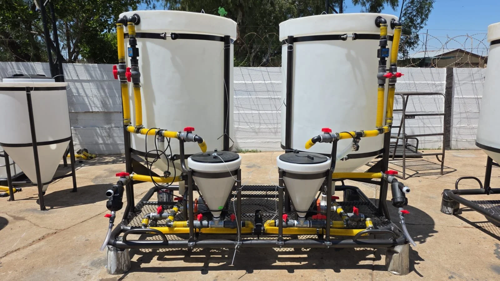 Powdery blue and white water treatment equipment with yellow pipes, red valves, black frames, and a concrete flooring outdoors.