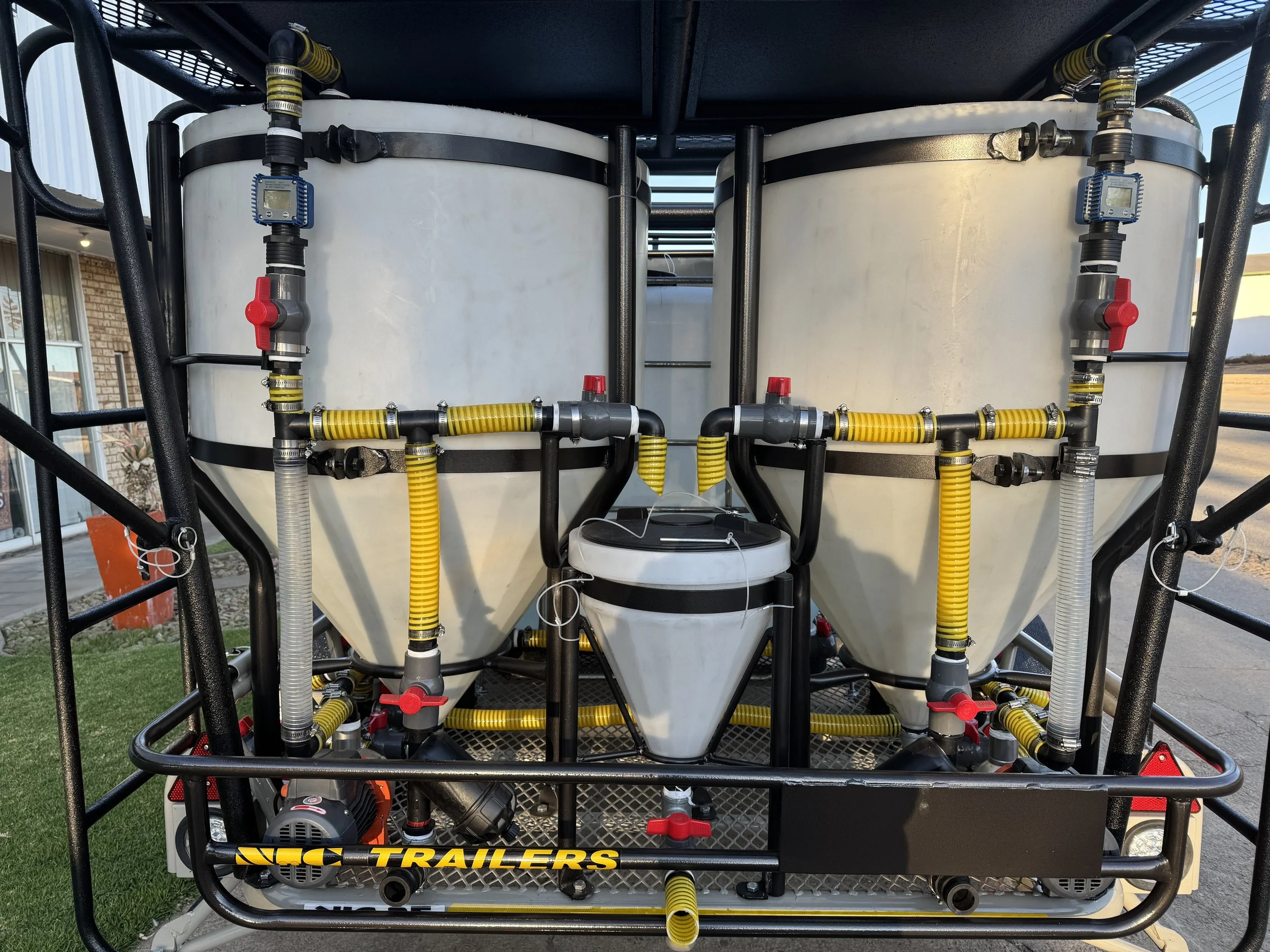 Two large white tanks connected by black and yellow pipes with red valve handles, mounted on a metal frame with a sign labeled 'TRAILERS' in yellow letters.