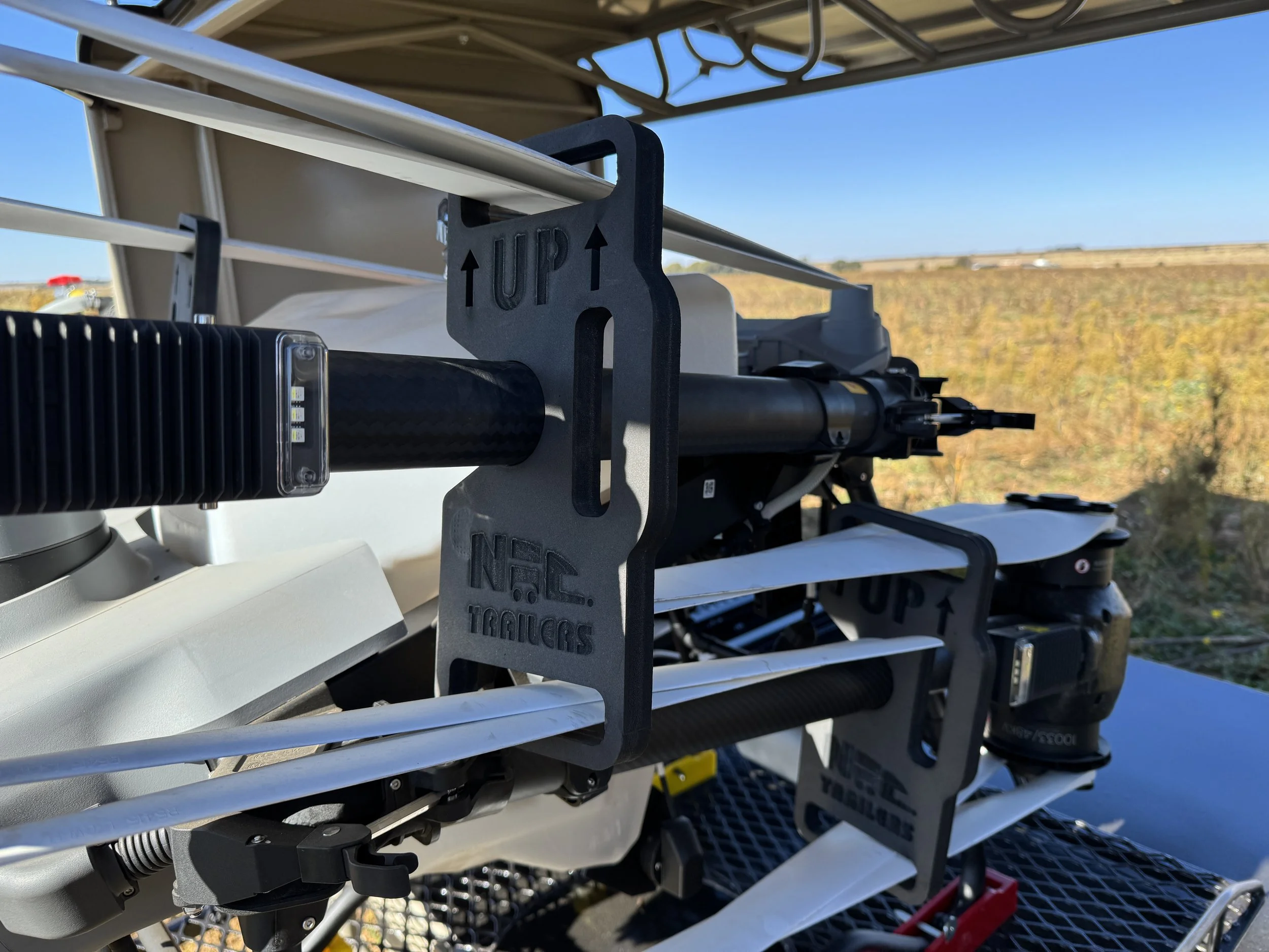 Close-up of a drone's camera and gimbal system, with a background of open farmland and a clear blue sky.