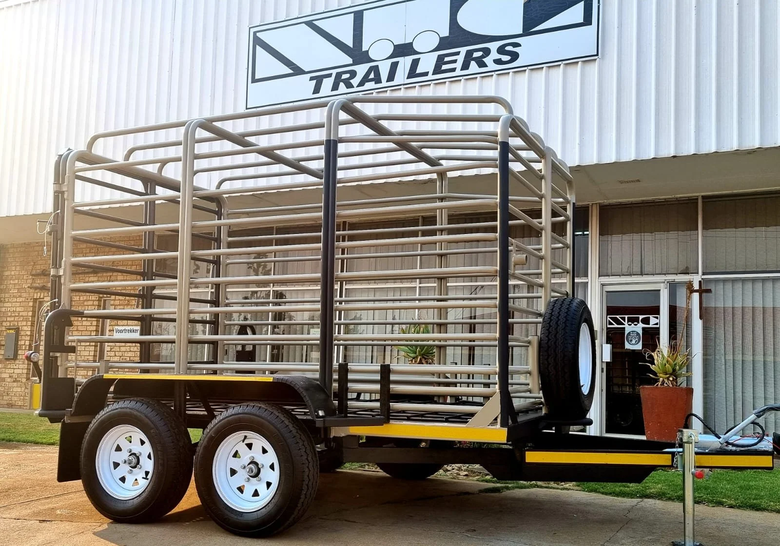 Enclosed livestock trailer with metal bars parked outside a trailer dealership.