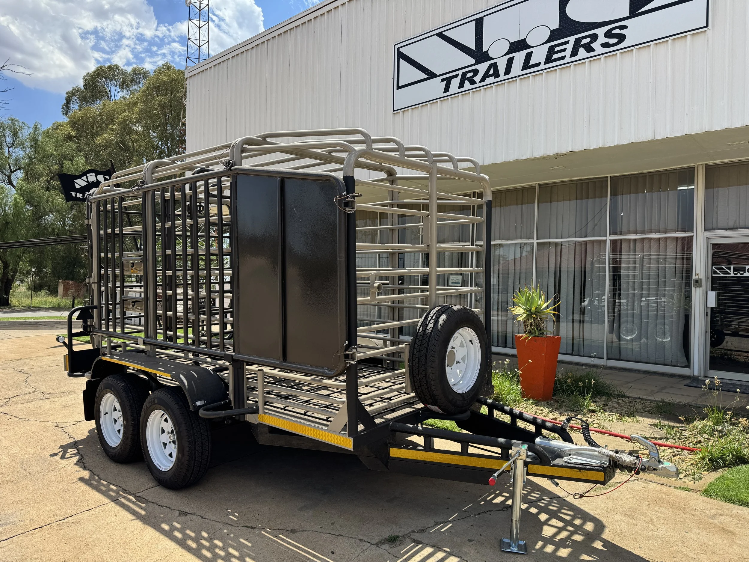 A flatbed livestock trailer with a metal cage and spare tire