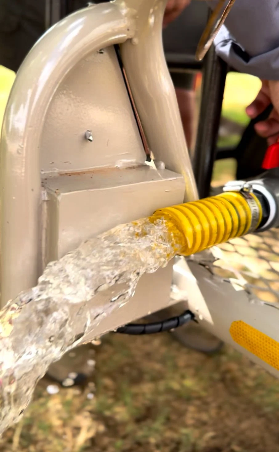 Water being poured through a yellow hose connected to a manual water pump outdoors.