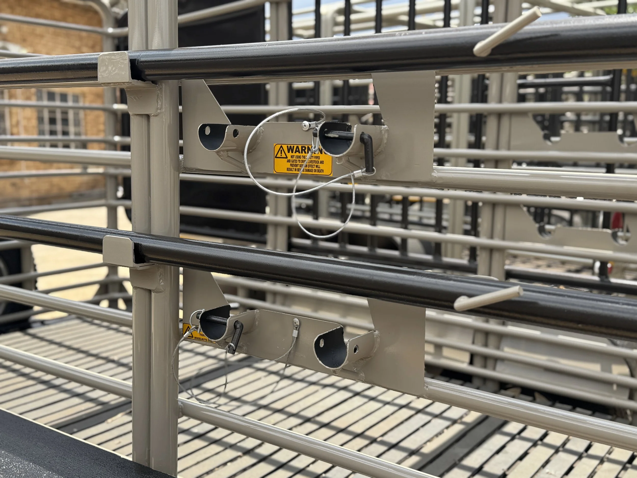 Close-up of a metal livestock gate with a warning label, outdoor setting.