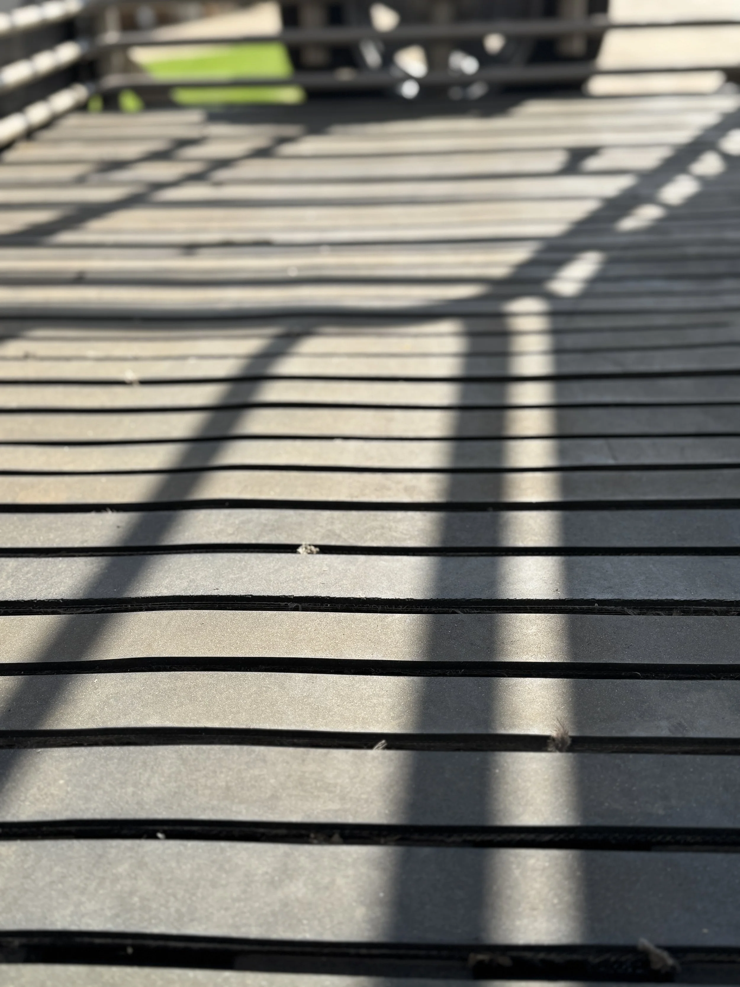 Shadows of a metal railing cast on a wooden surface.