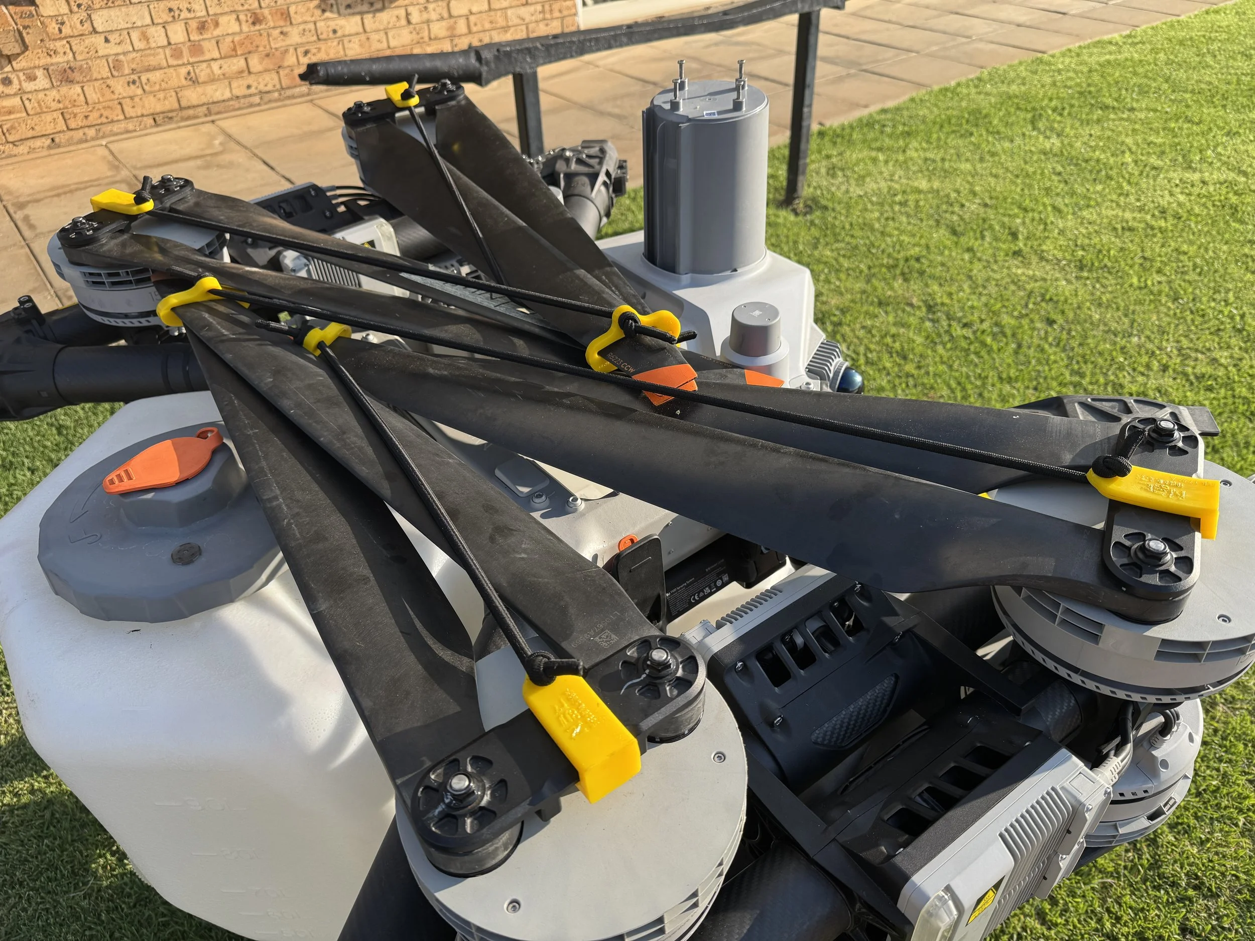 Close-up of a drone with four propellers, showing details of the motors, propellers, and electronic components on a grassy lawn.