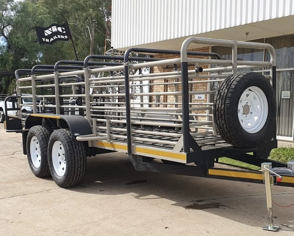 Livestock trailer with dual axles and side rails, parked outdoors, with a spare tire attached.
