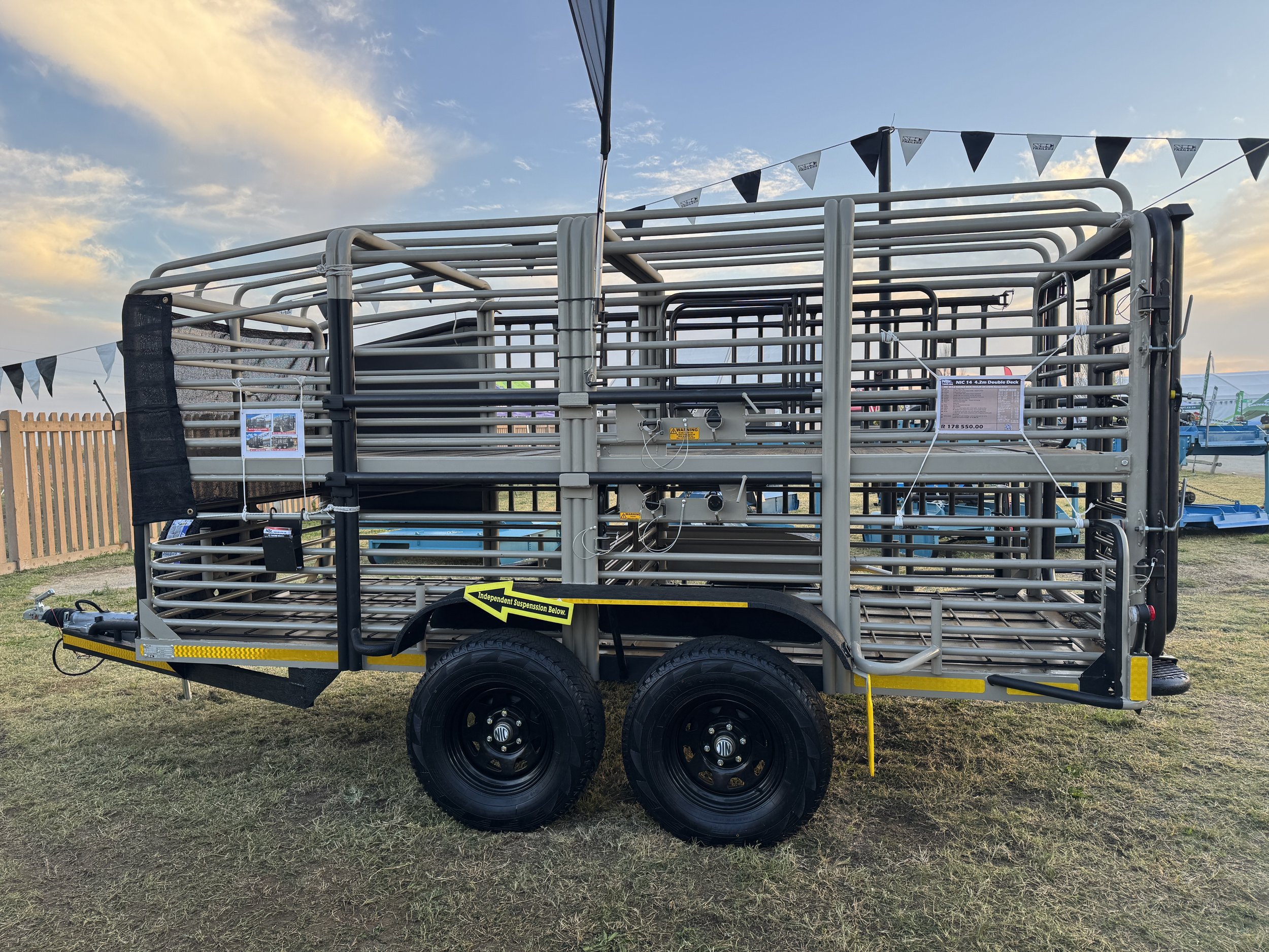 A large farm trailer with metal bars on a grassy field at sunset, with black and white flags hanging above.