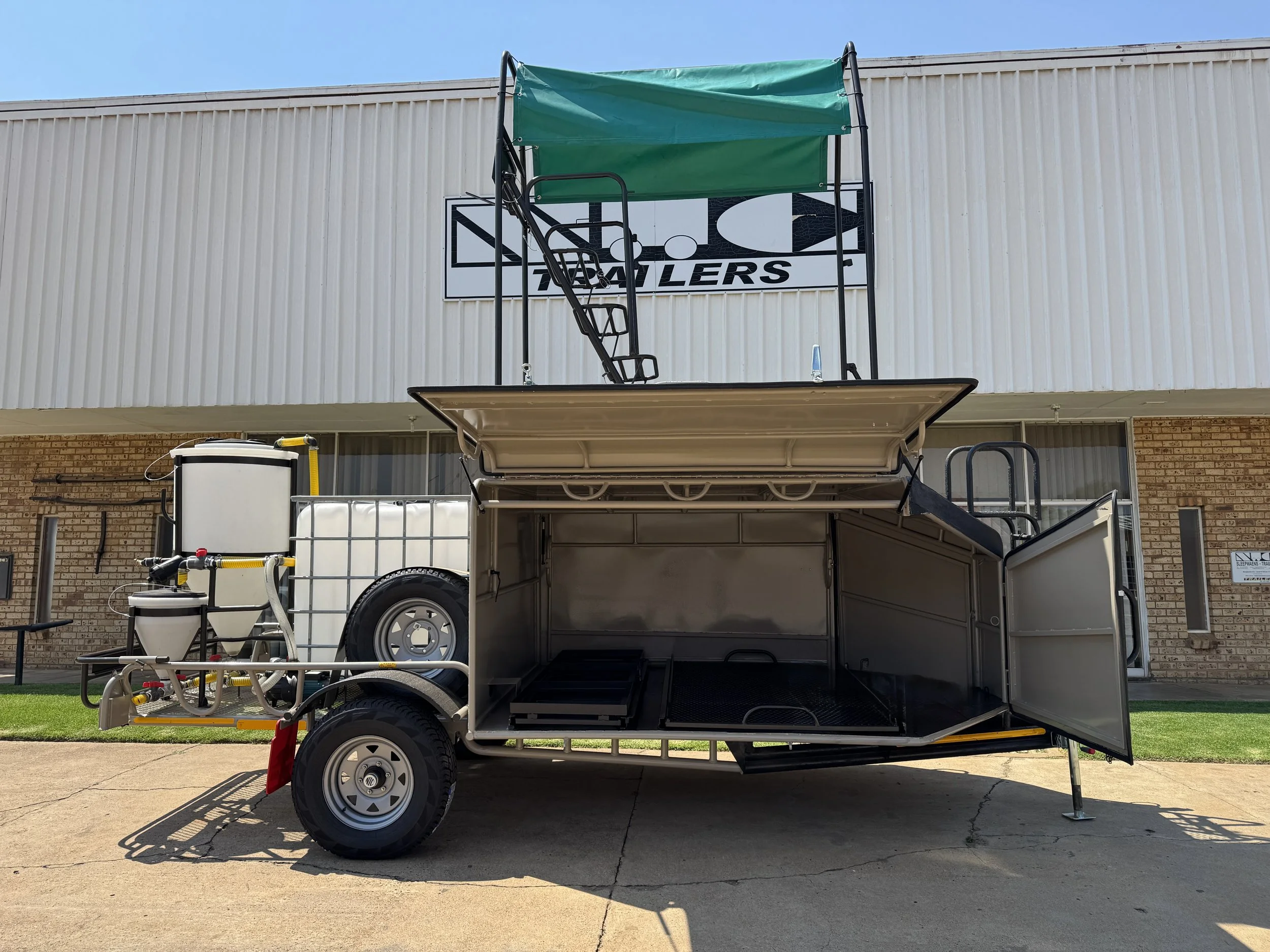 A specialized mobile trailer with open compartments and equipment, parked outside a building with a sign that reads 'Trailers' and an image of a fish.