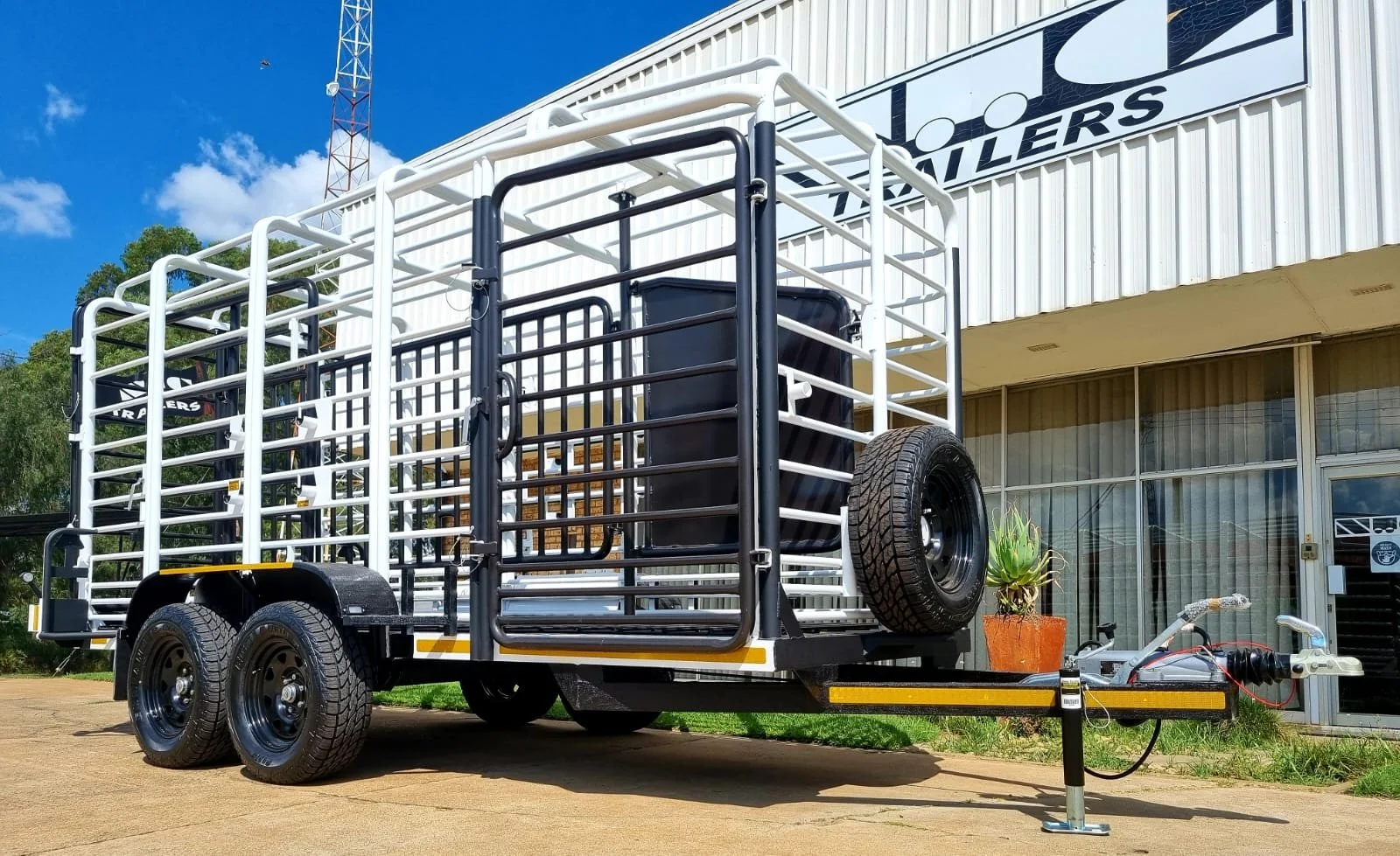 Heavy-duty cattle trailer with dual wheels and metal framework parked outside a building.