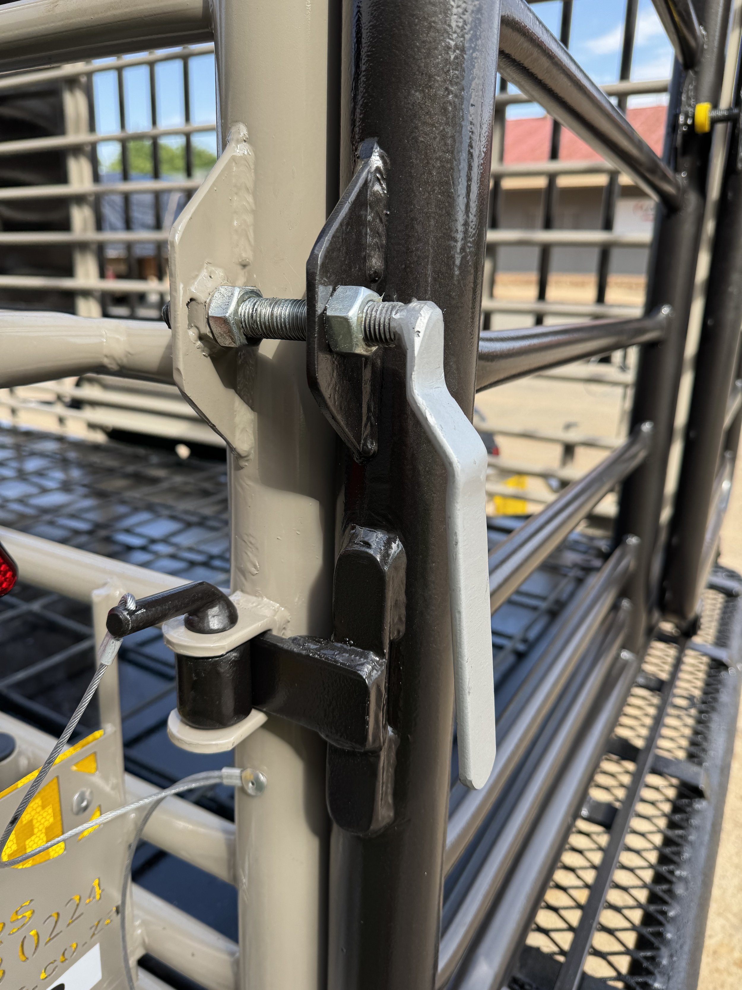Close-up of a metal latch mechanism on a gate with bolts and a hinge.