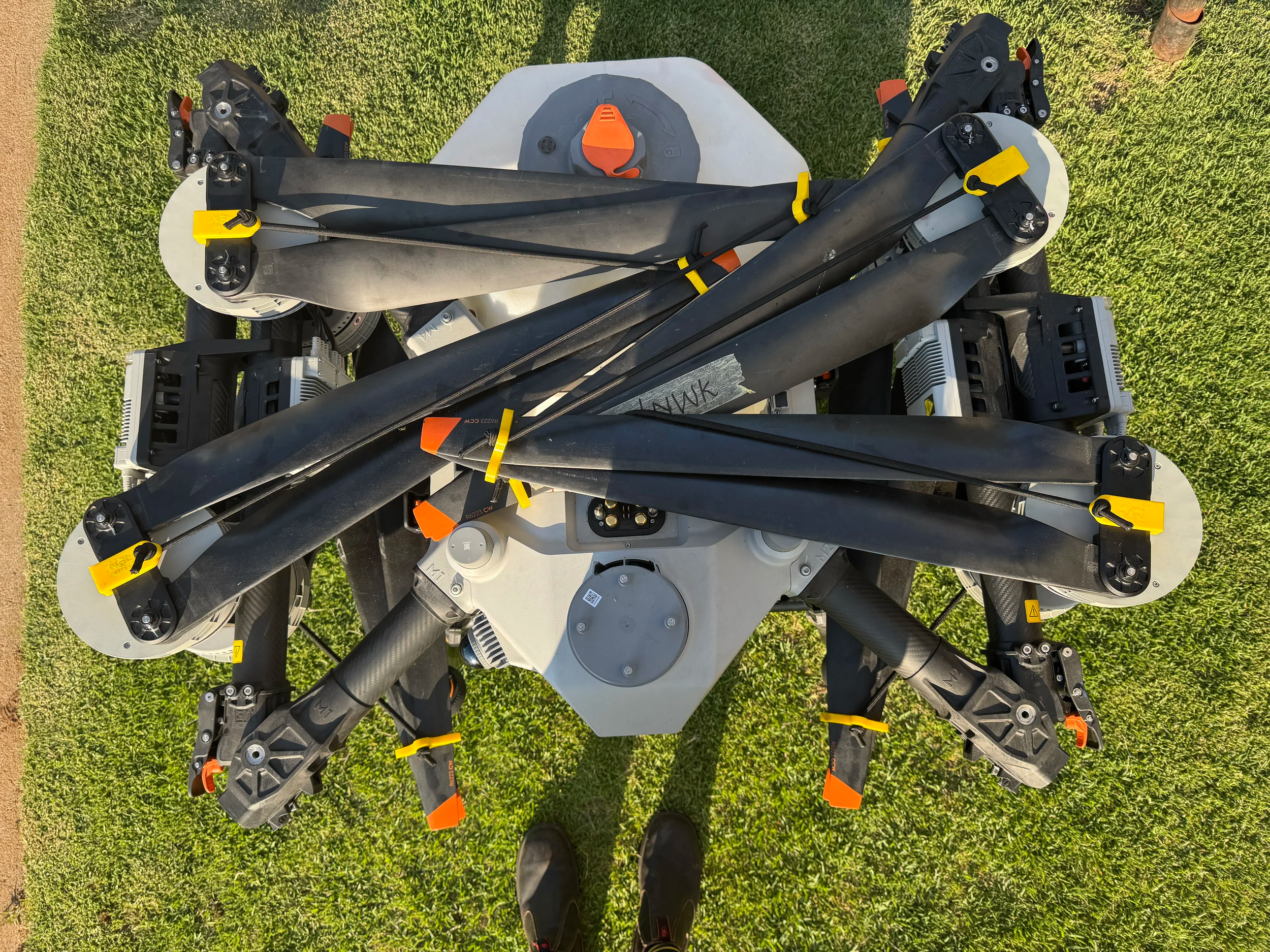 A drone frame with multiple arms and motors, placed on grass, with black and orange components and a central gray body.
