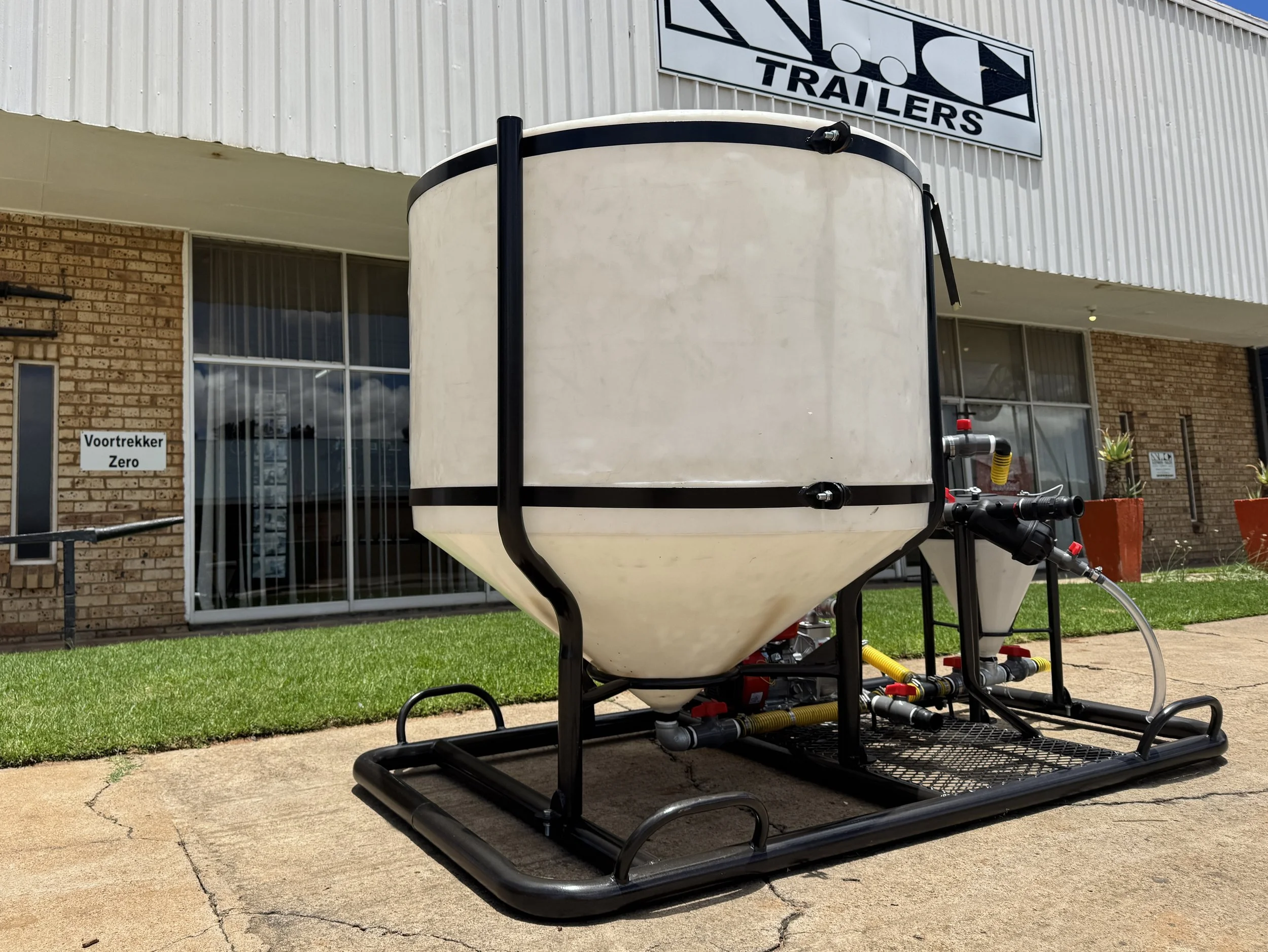 Large white tank with black frame, connected pipes, placed on a black metal platform outside a commercial building.